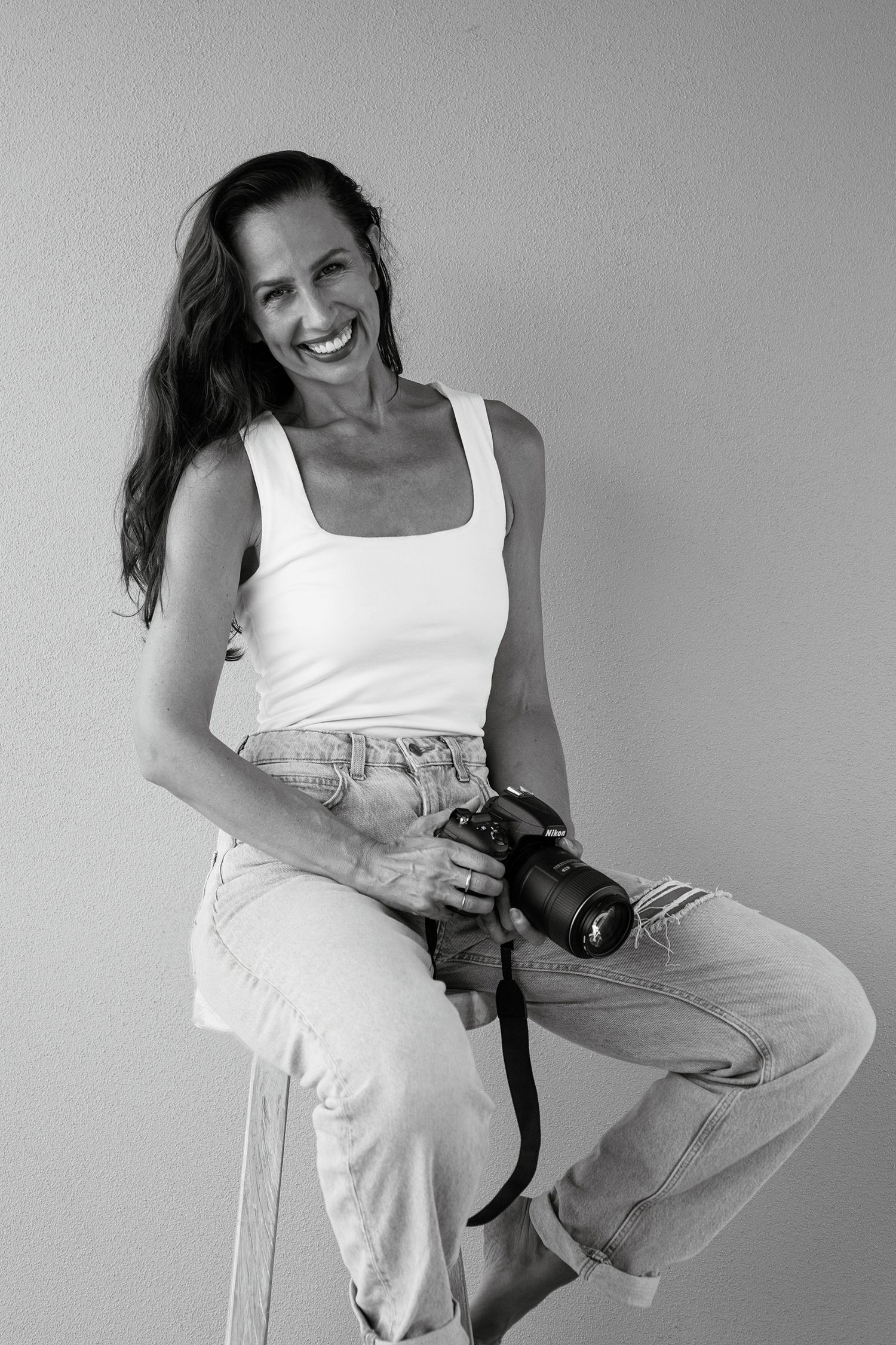Black and white photo series of model in white tank top and jeans posing with camera.