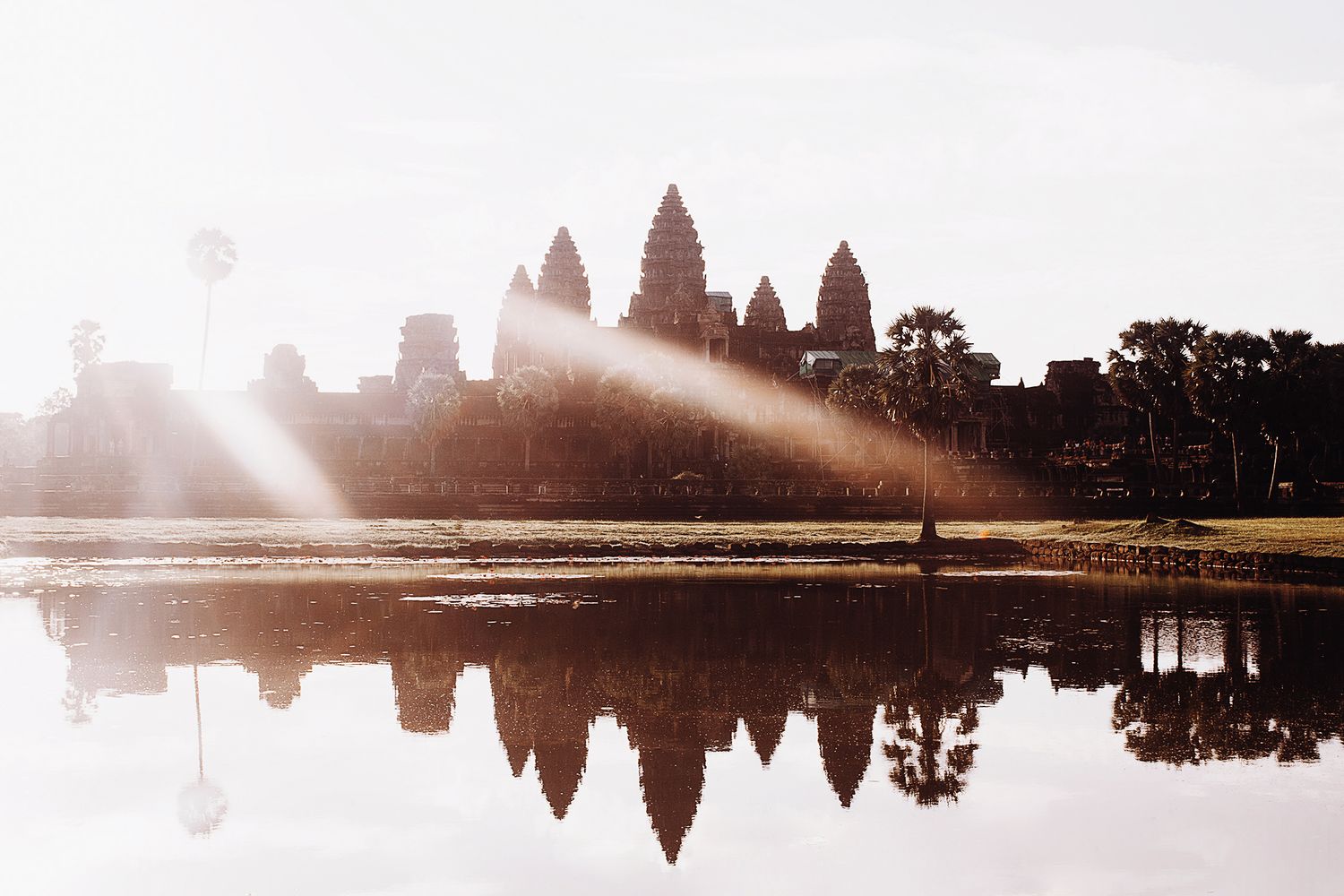 Panoramic silhouette of Angkor Wat temple reflected in still water during misty sunrise in Cambodia.