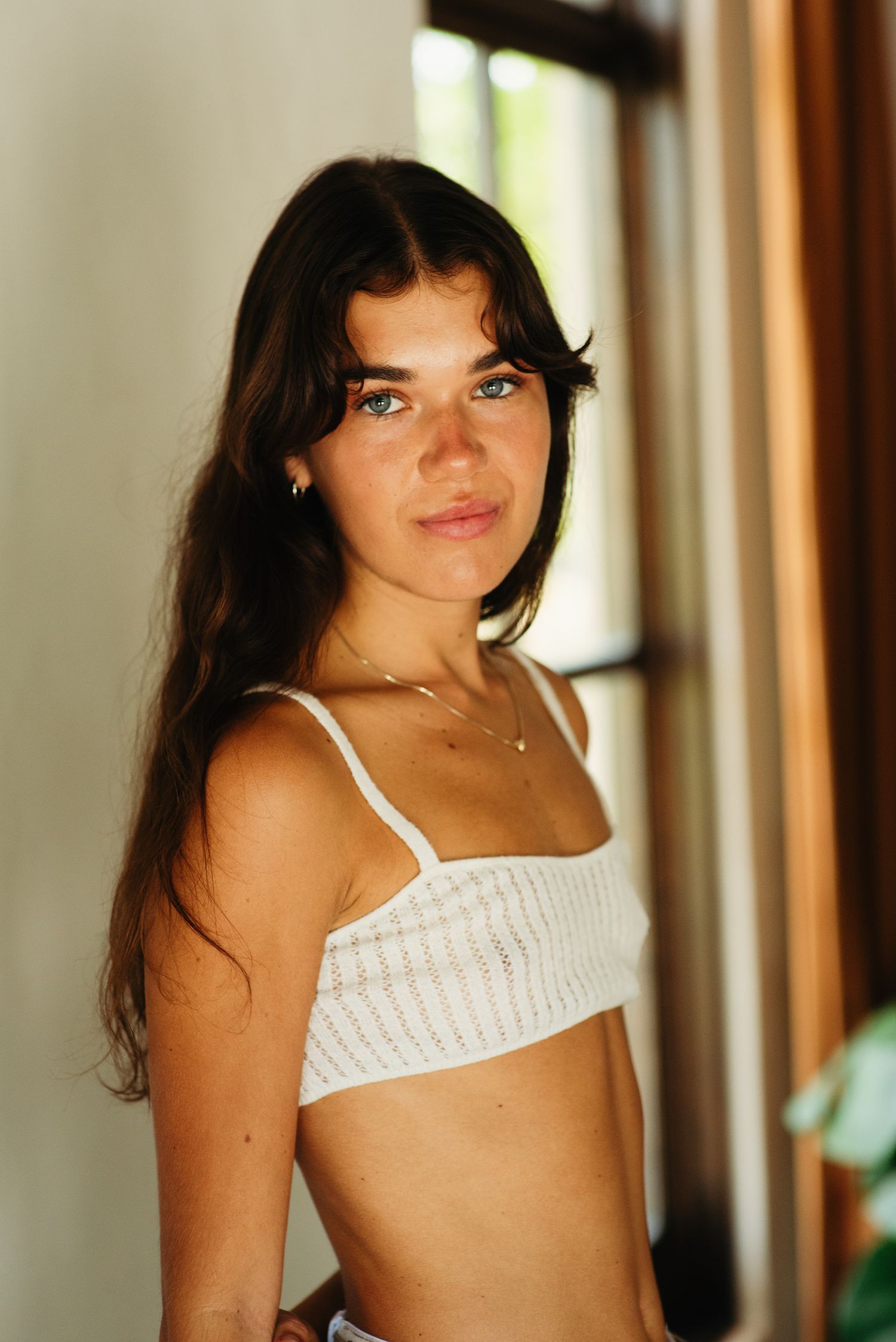 Indoor portrait series showing someone posing in white summer top against neutral background.