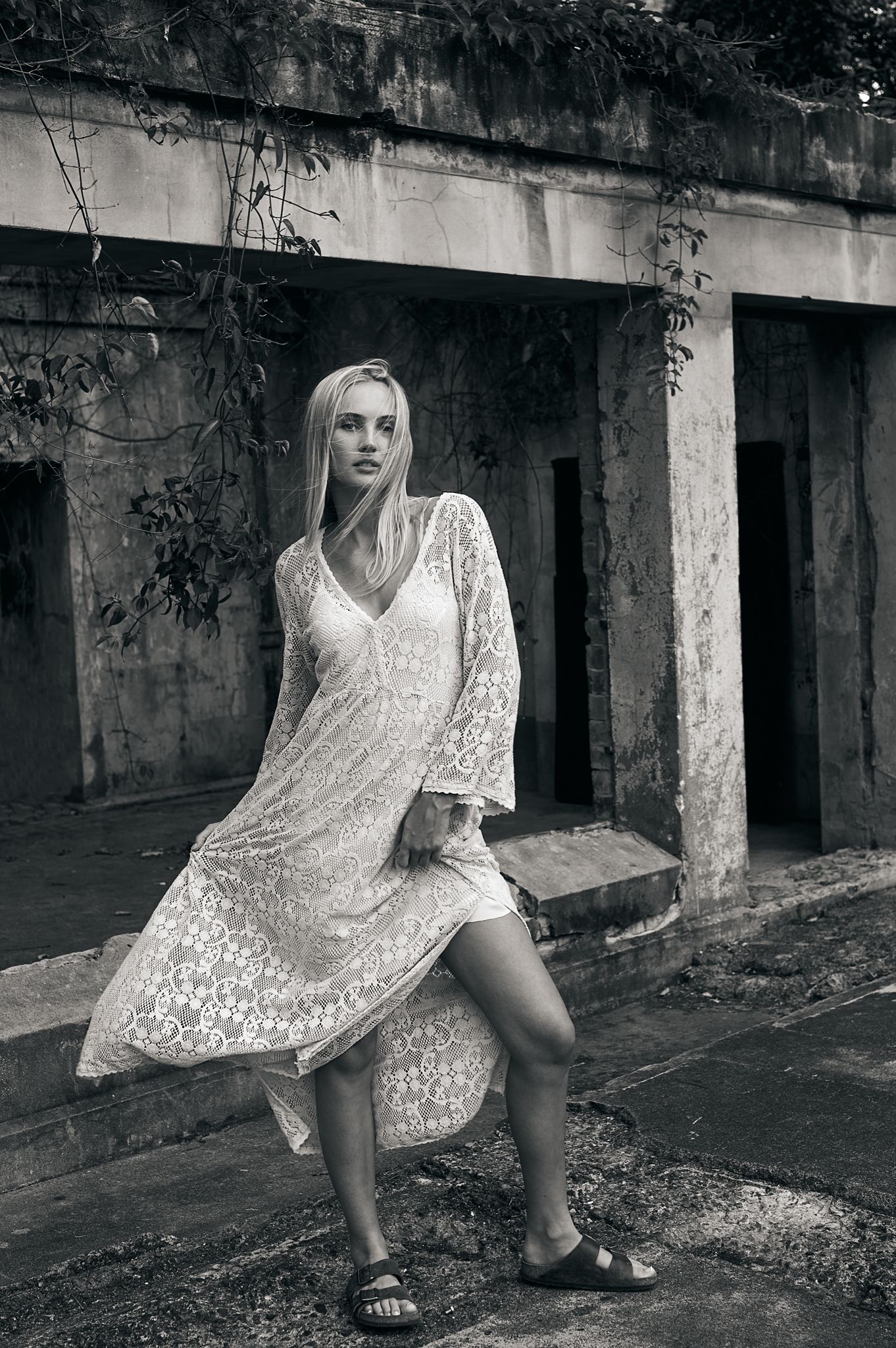 A series of black and white fashion photos showing a figure in a white lace dress against an industrial concrete backdrop.