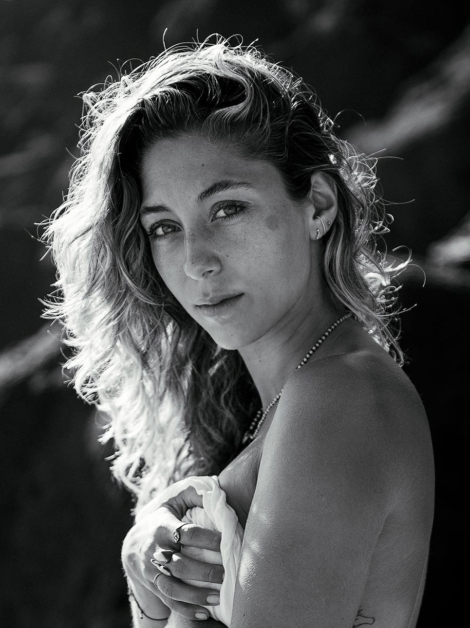 Black and white portrait of a woman with windswept hair looking over her shoulder in natural lighting.