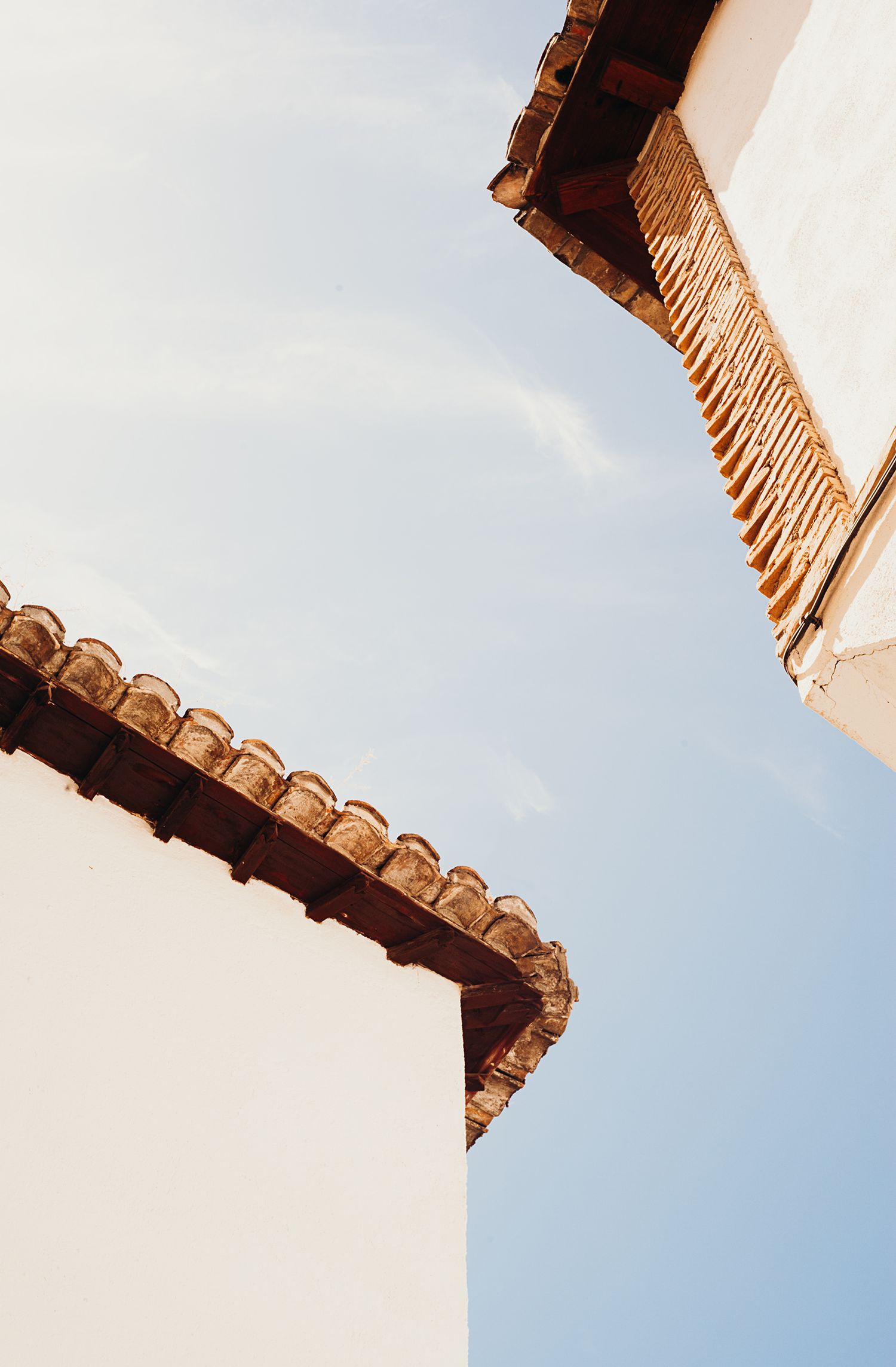 Architectural detail of white Spanish-style building with terracotta roof tiles against bright blue sky.