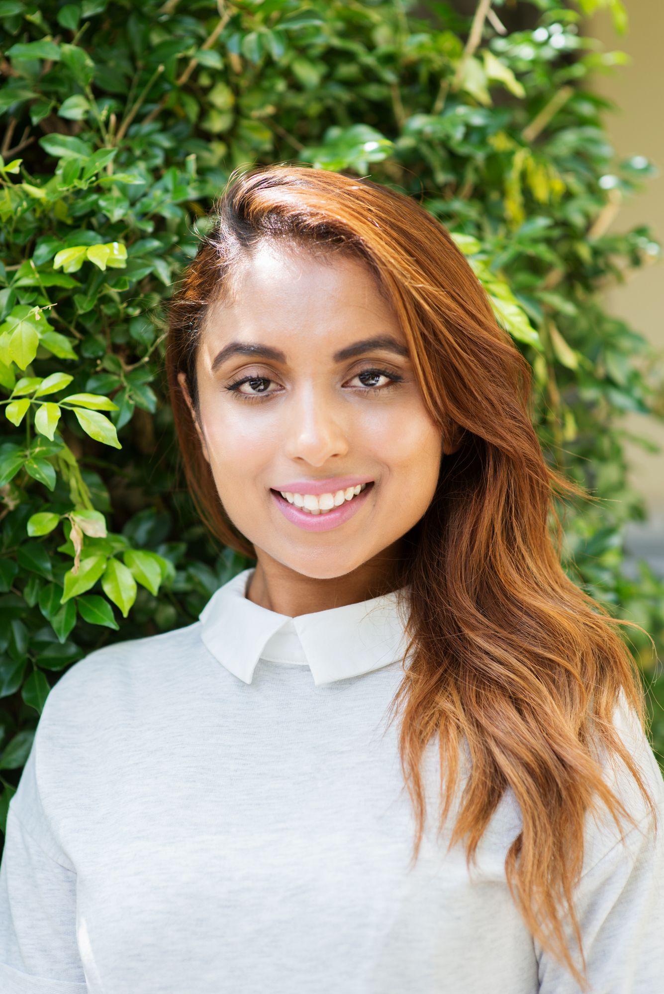 Outdoor portrait with lush green foliage background wearing light colored top.