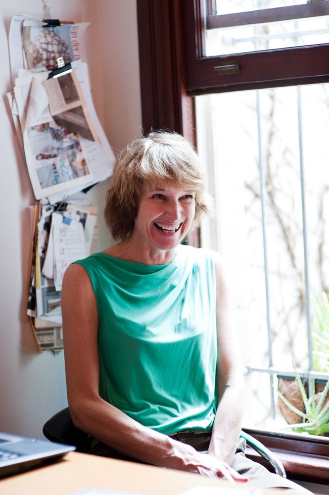 Woman in turquoise sleeveless top sits by window in casual indoor photoshoot series.