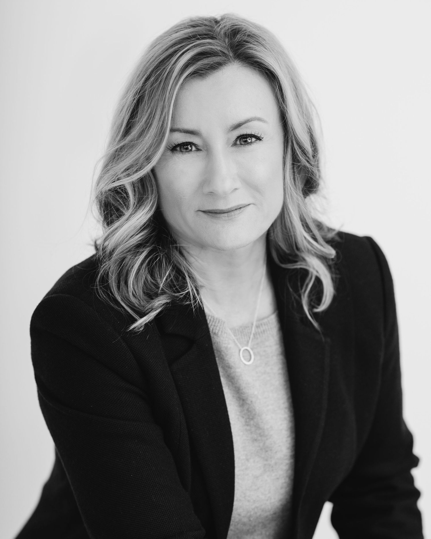 Professional black and white headshot series showing confident pose in black blazer against light background.