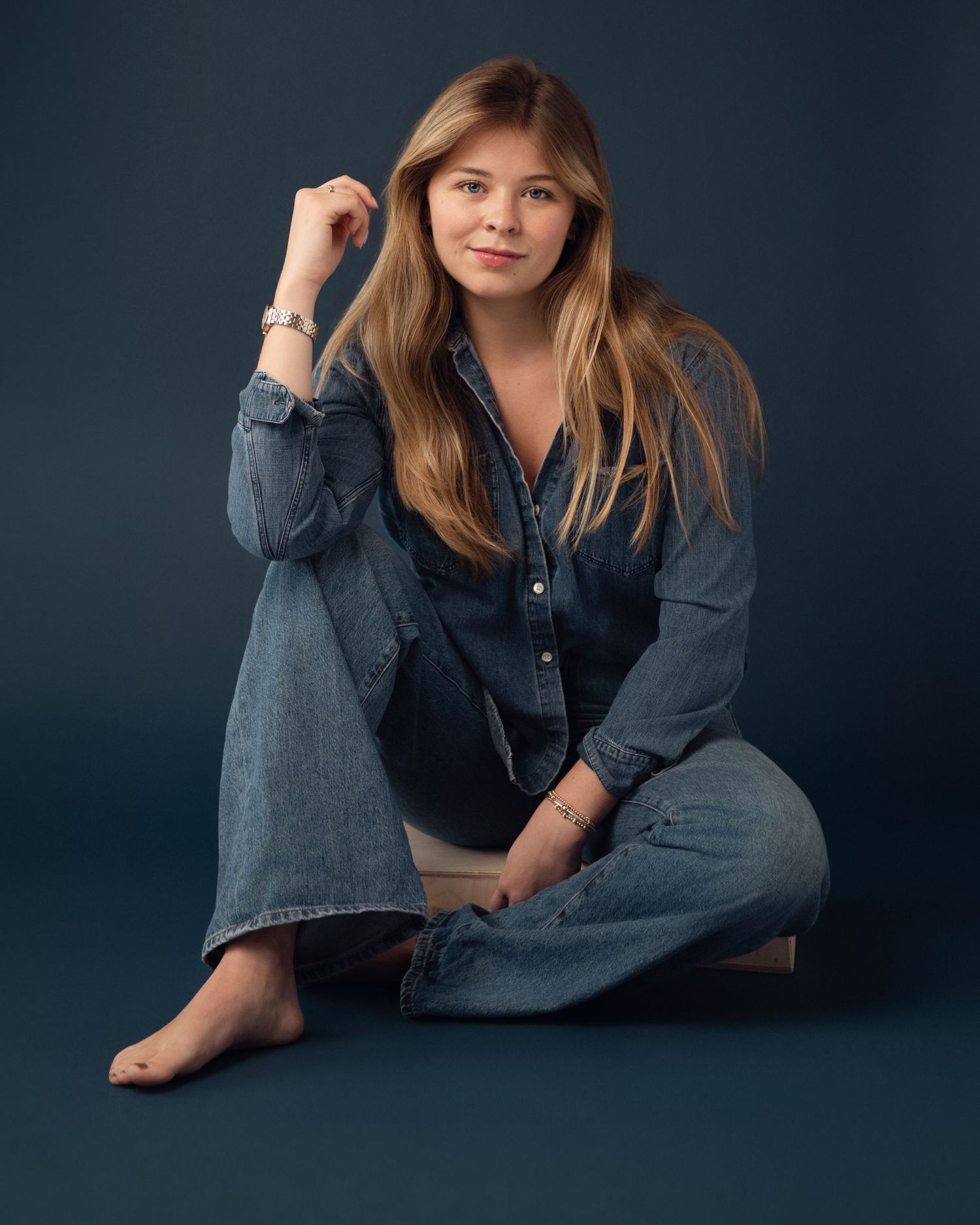 Casual portrait series featuring relaxed poses in denim against a deep blue backdrop.