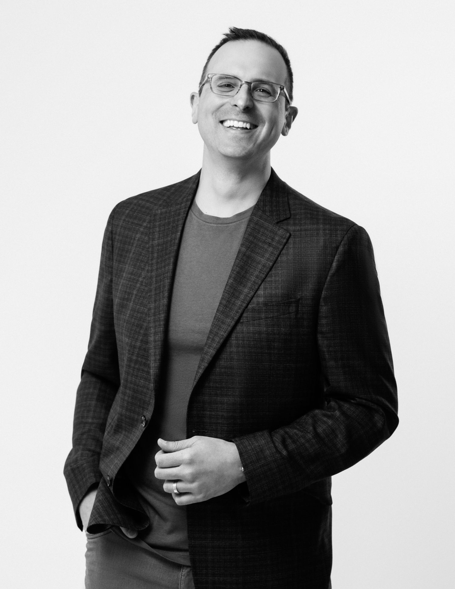 Professional headshot of person in glasses and blazer smiling against white background.