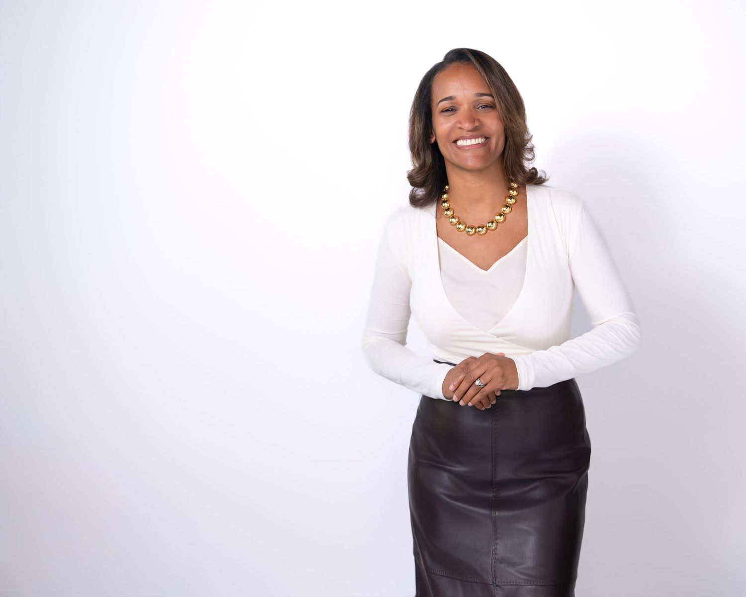 Professional wearing a white top and black leather skirt poses confidently against a light background.