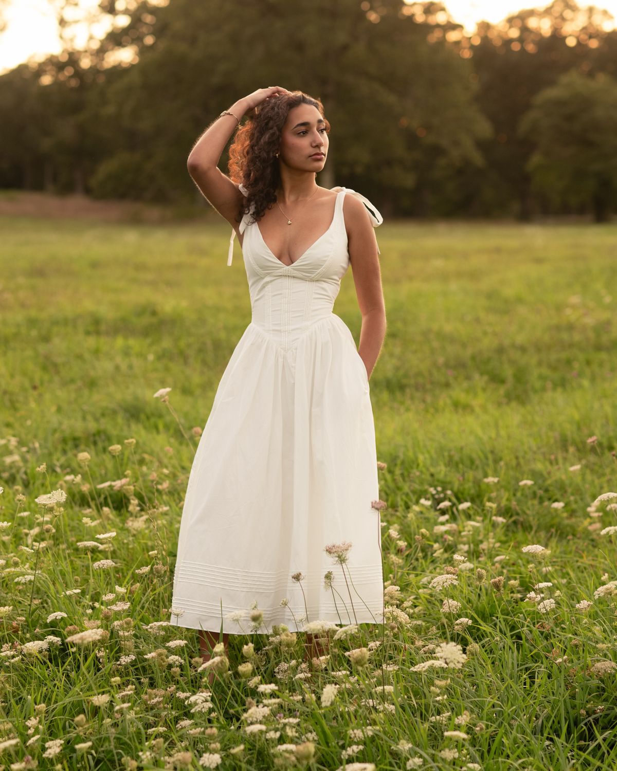 Woman in white sundress walking through meadow with wildflowers at golden hour.