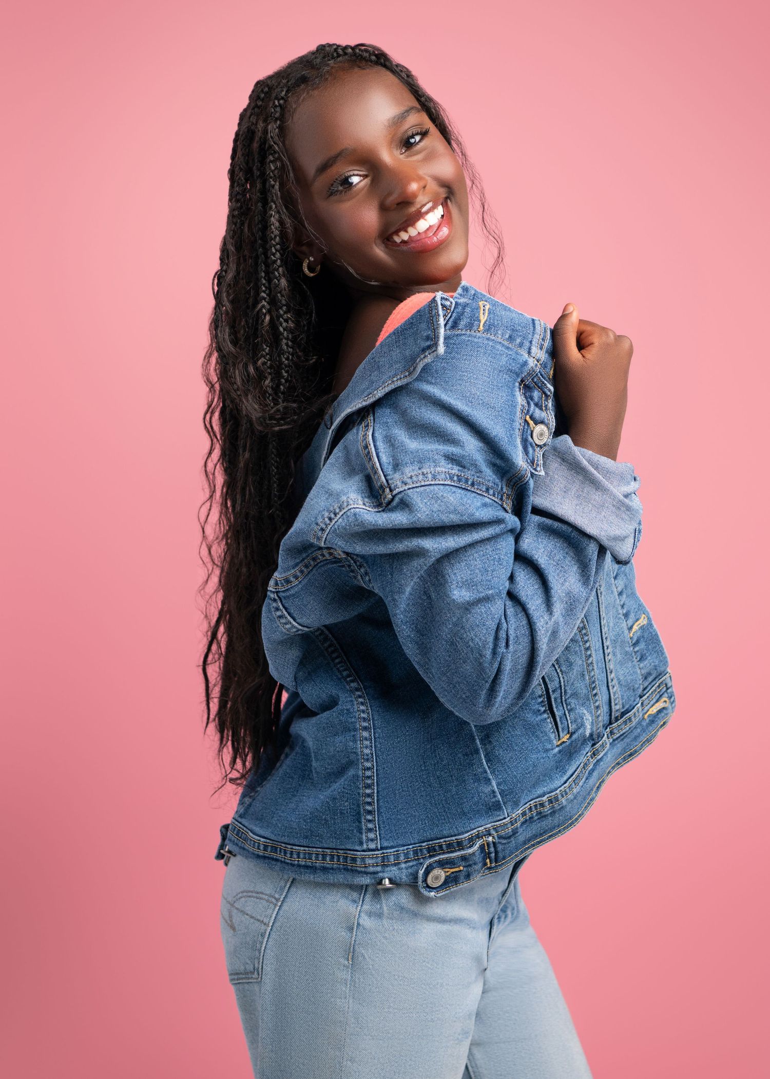 Playful fashion poses in denim jacket against pink background.