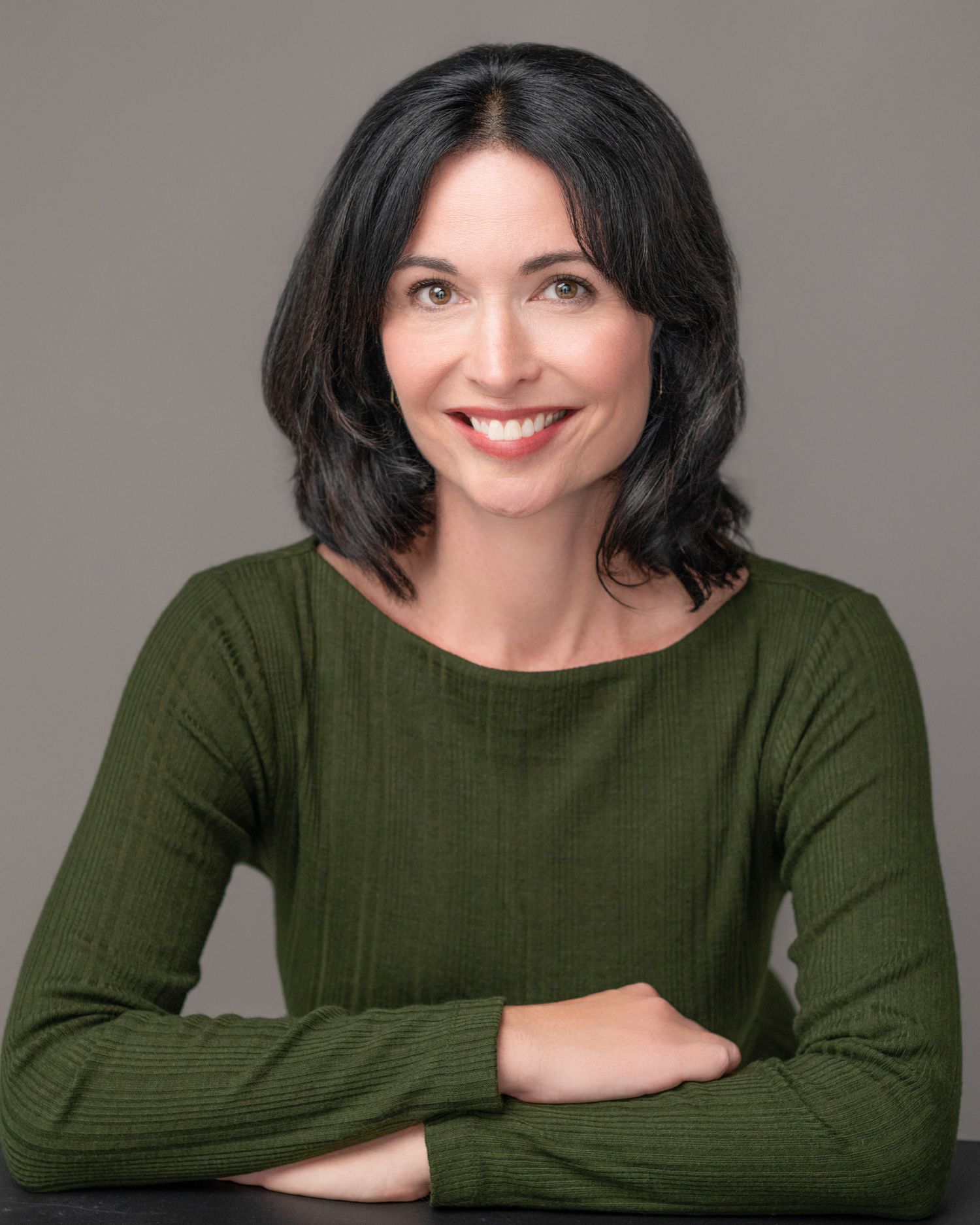 Portrait of a person in an olive green sweater with crossed arms.