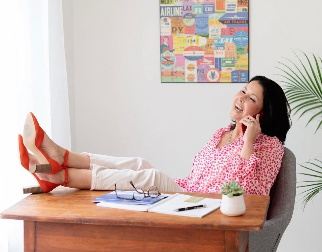 Person relaxing with feet up on desk in bright office space with colorful wall art and tropical plant decor. Realtor Branding Seacoast NH