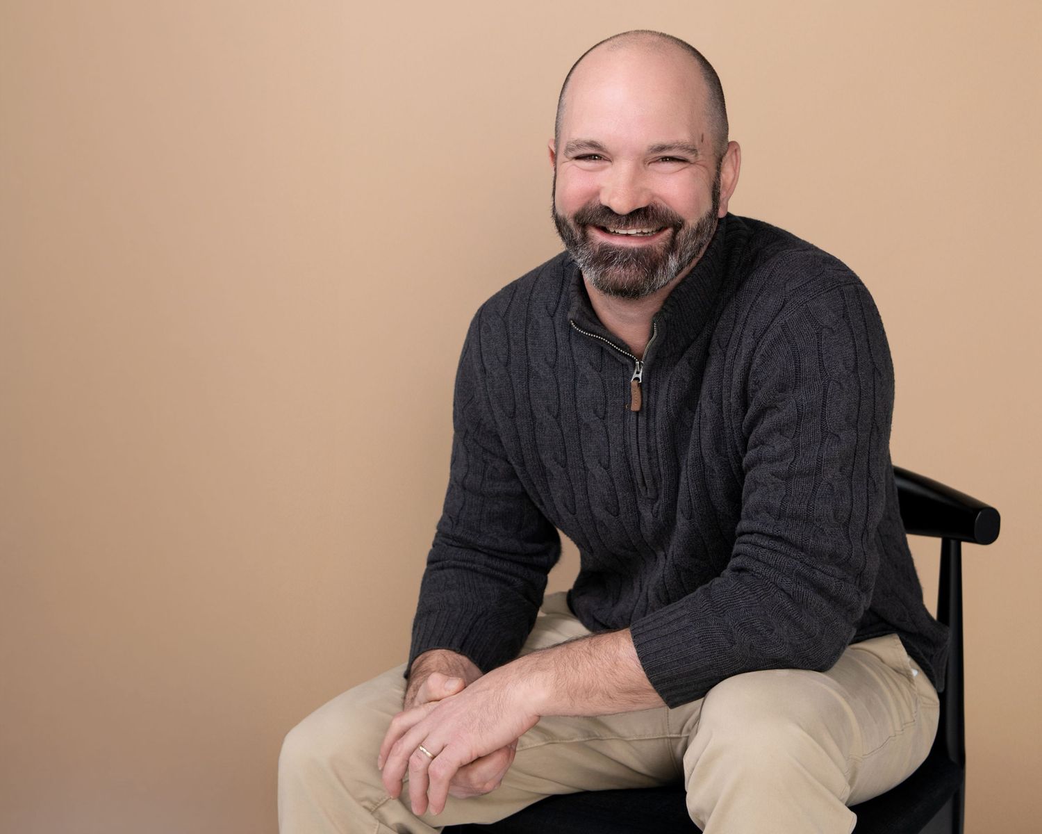 Studio portraits of person in black sweater against beige background.