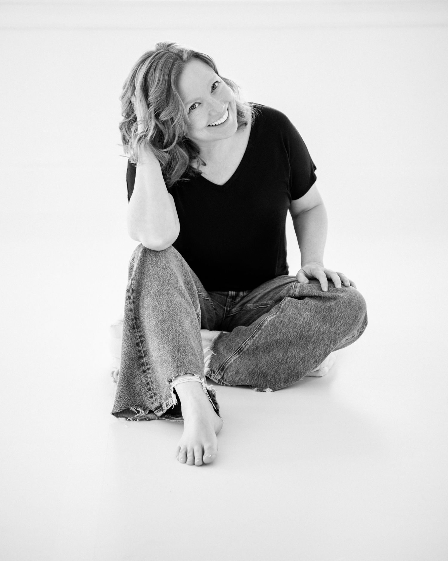 Black and white artistic portrait series showing a casual seated pose in jeans against white background.