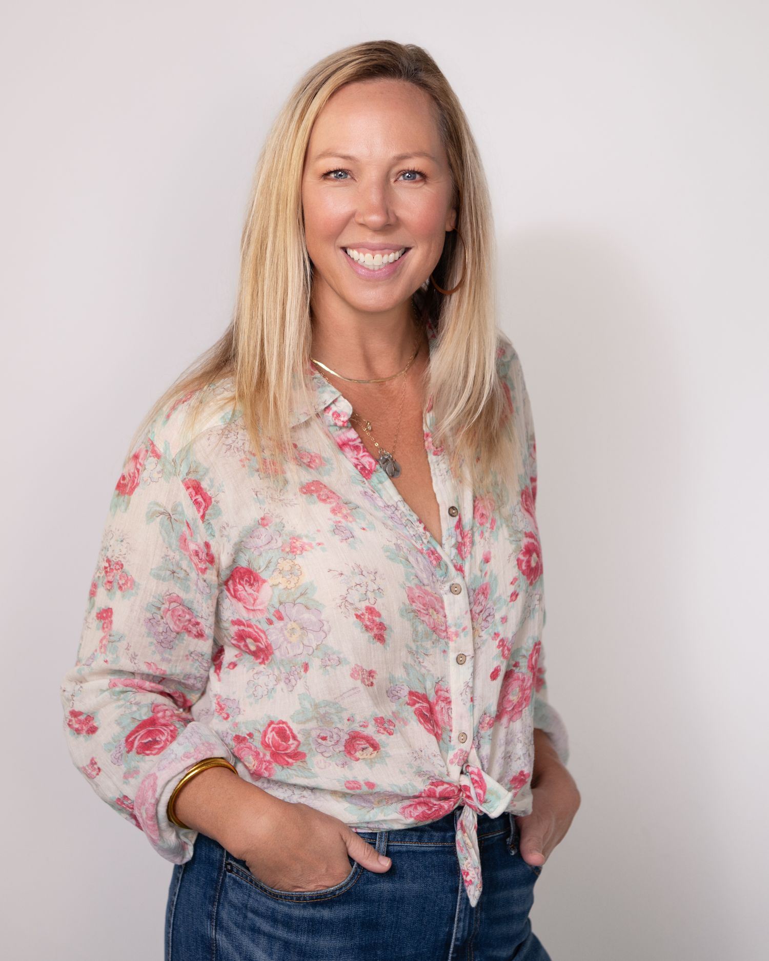 Model in floral print blouse and denim poses against white studio background.