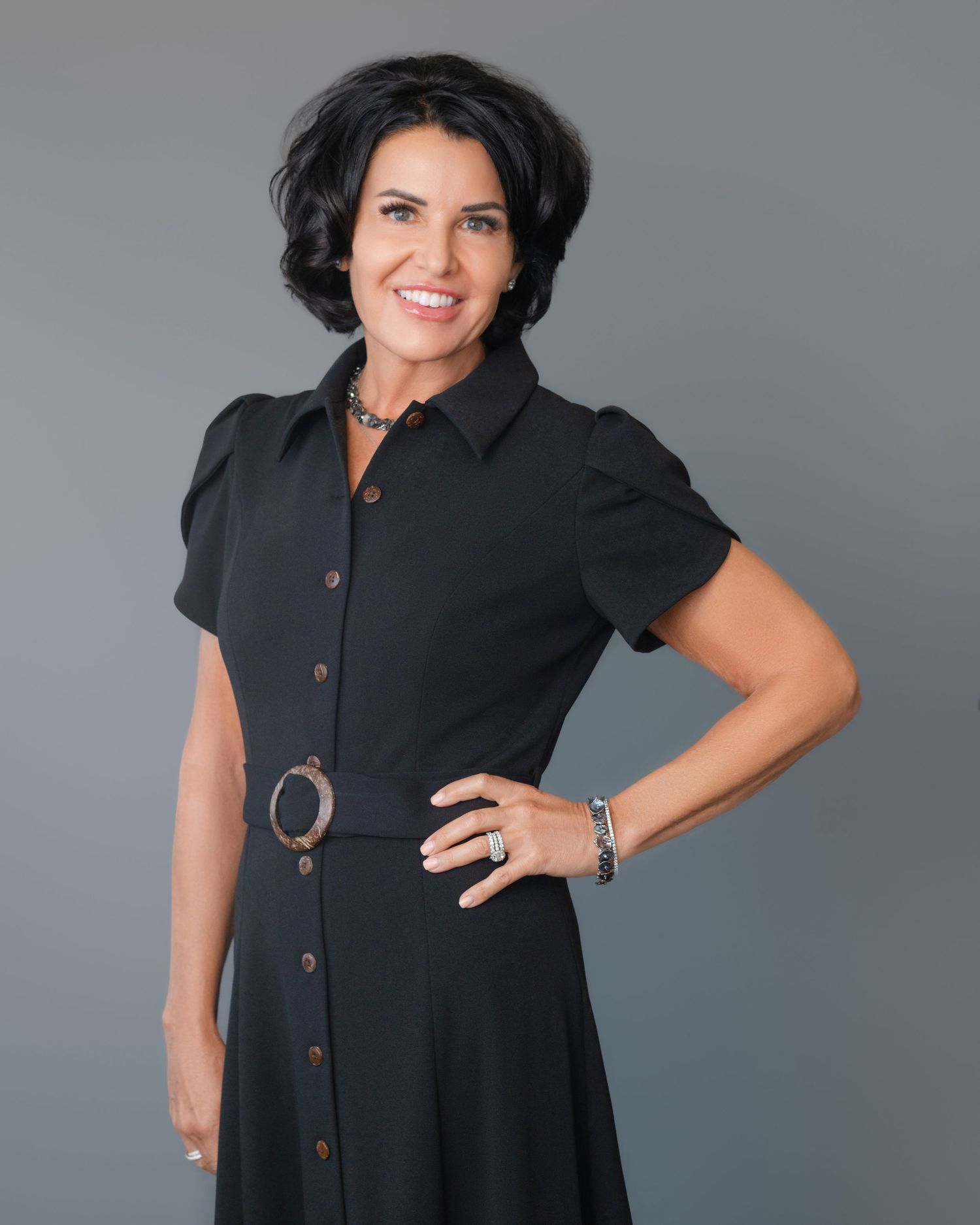 Professional portraits in a black button-down dress against a neutral gray background.