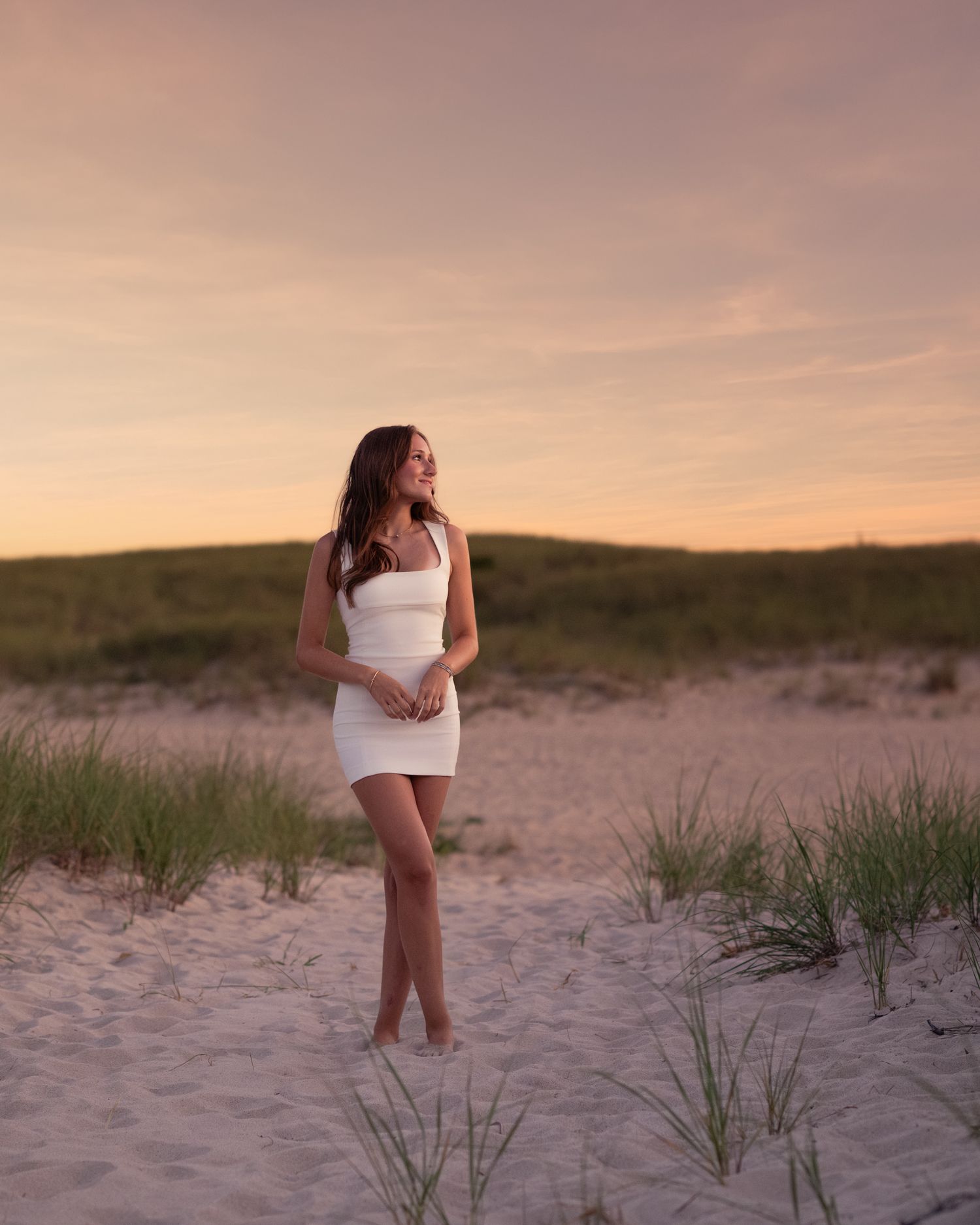 Sunset beach portrait in white dress among sand dunes.