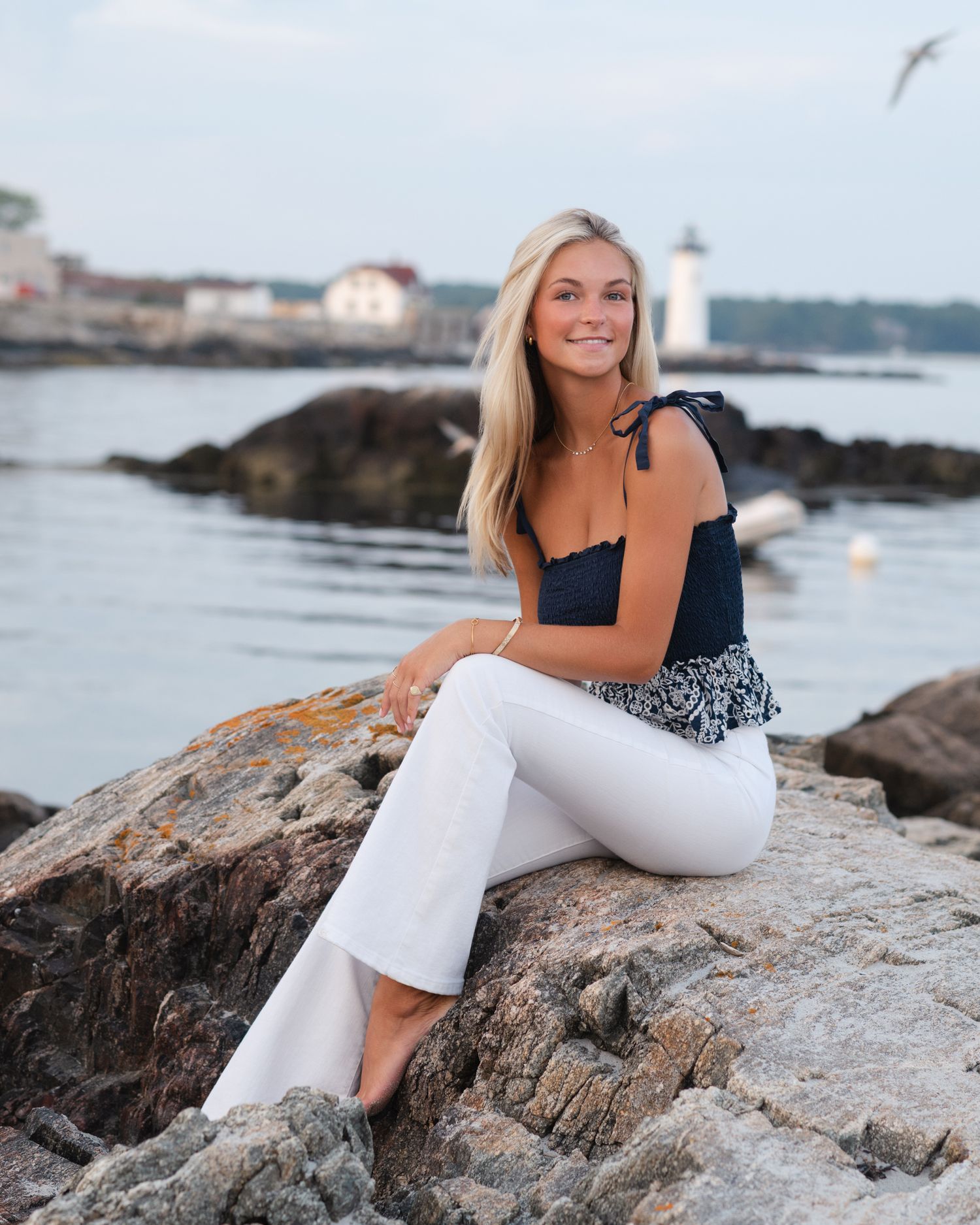 Summer portrait on coastal rocks with lighthouse and ocean in background.