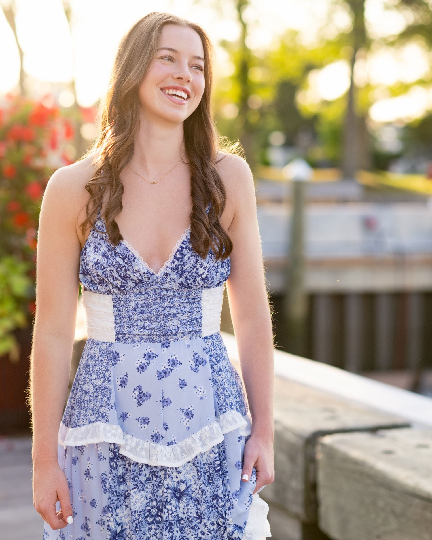 Woman in blue floral dress smiling during outdoor summer photoshoot.