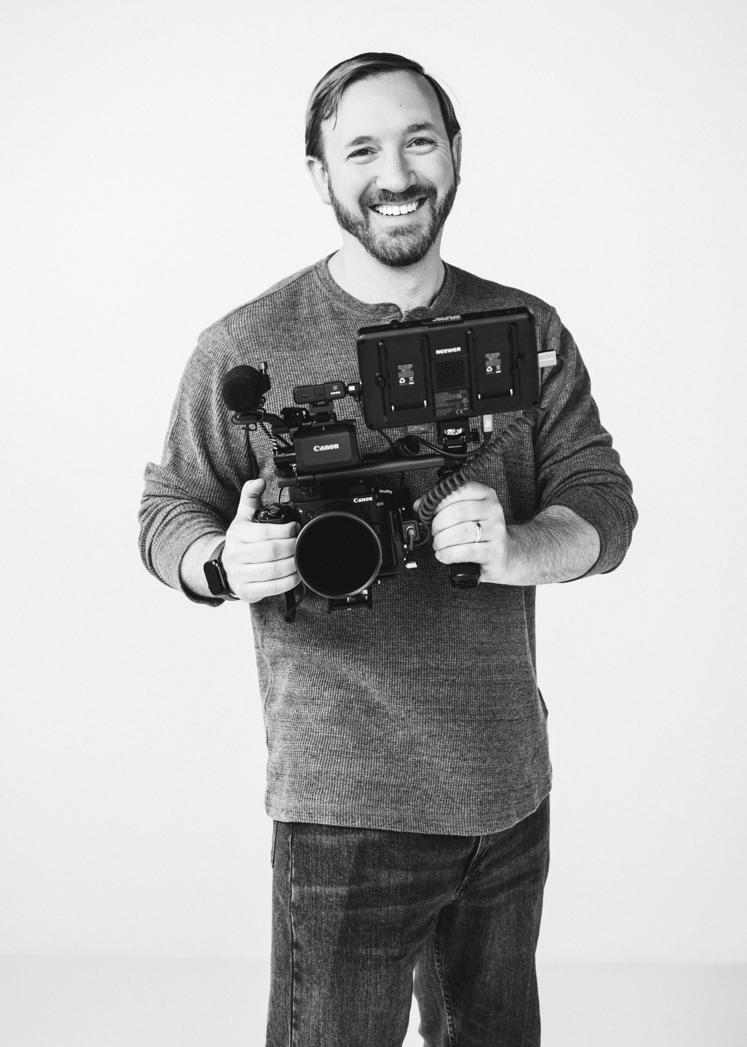 Smiling man holding a Canon professional video camera, black and white portrait photo.