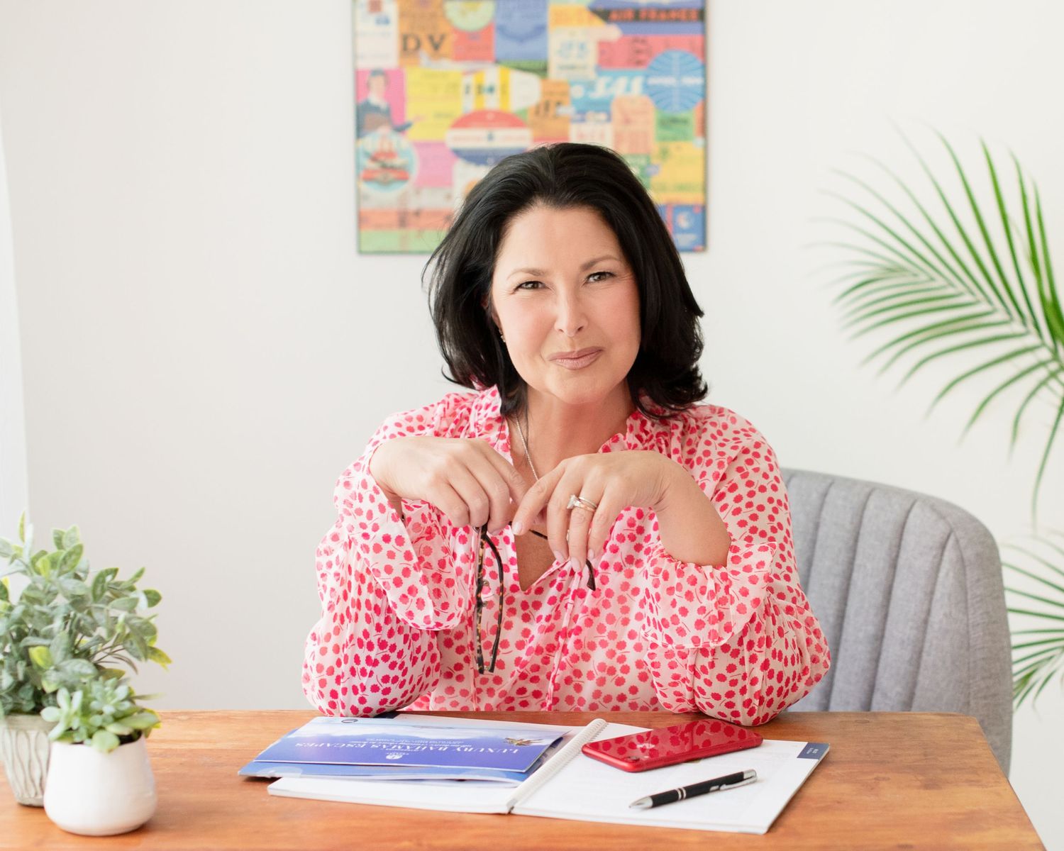 Professional sitting at desk wearing red polka dot blouse with colorful artwork and plants in bright office setting.