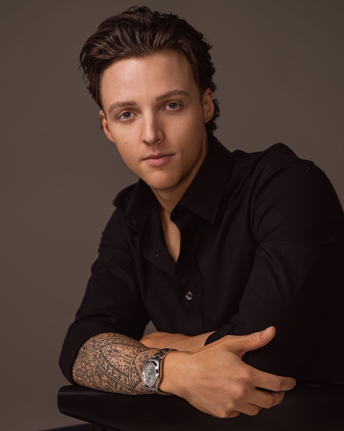 Professional studio portrait of a person in black shirt with tattoo sleeve and watch.