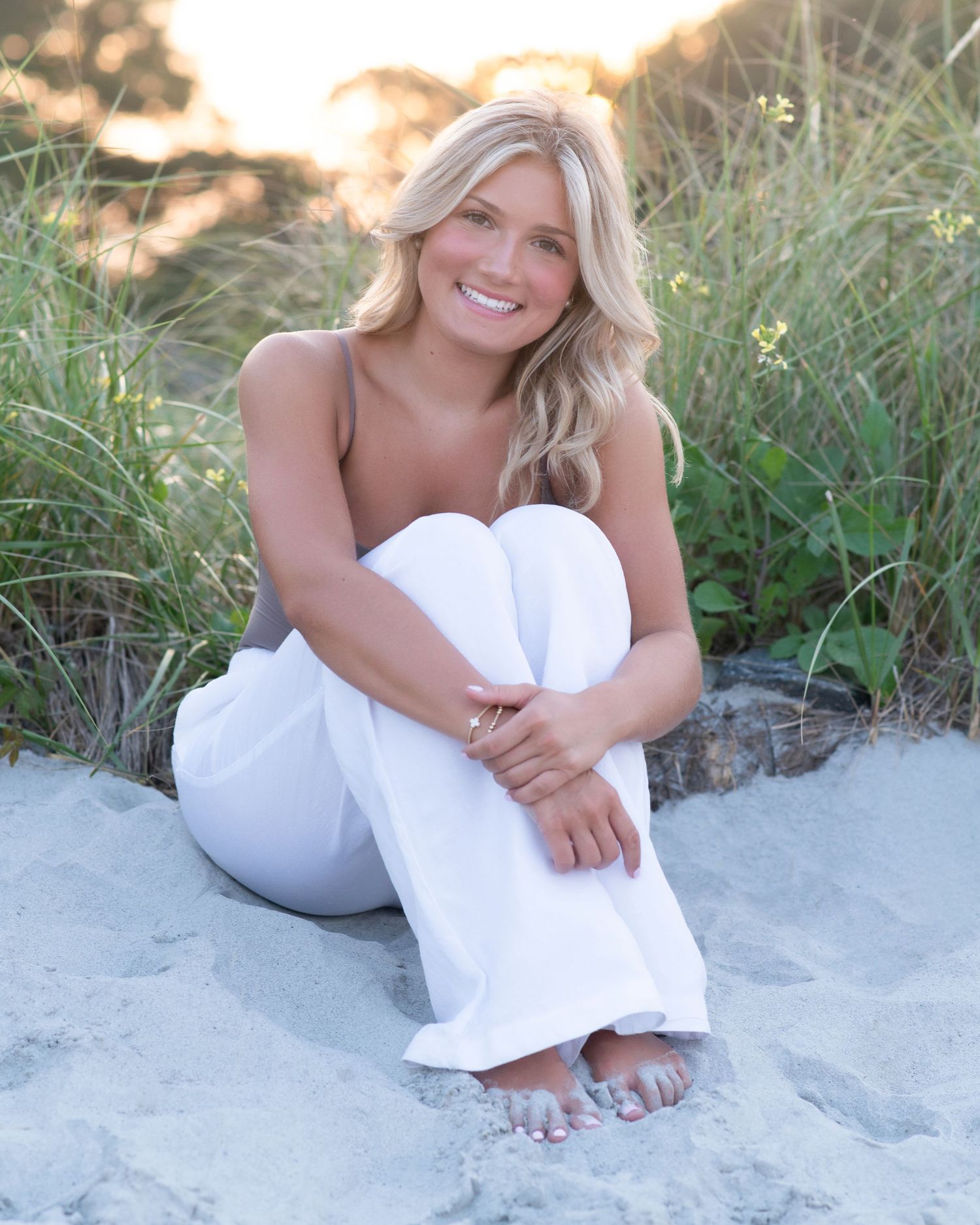 A relaxed beach portrait in white clothing against tall grass during golden hour.