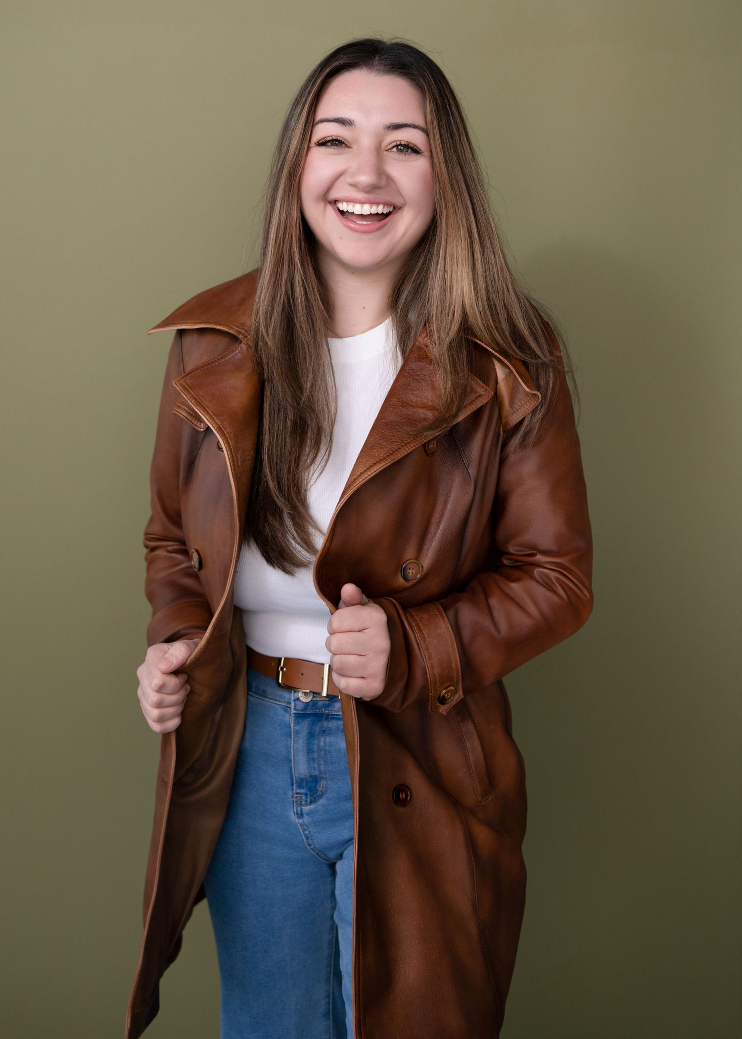 Style series featuring brown leather jacket with white top and blue jeans against olive background.