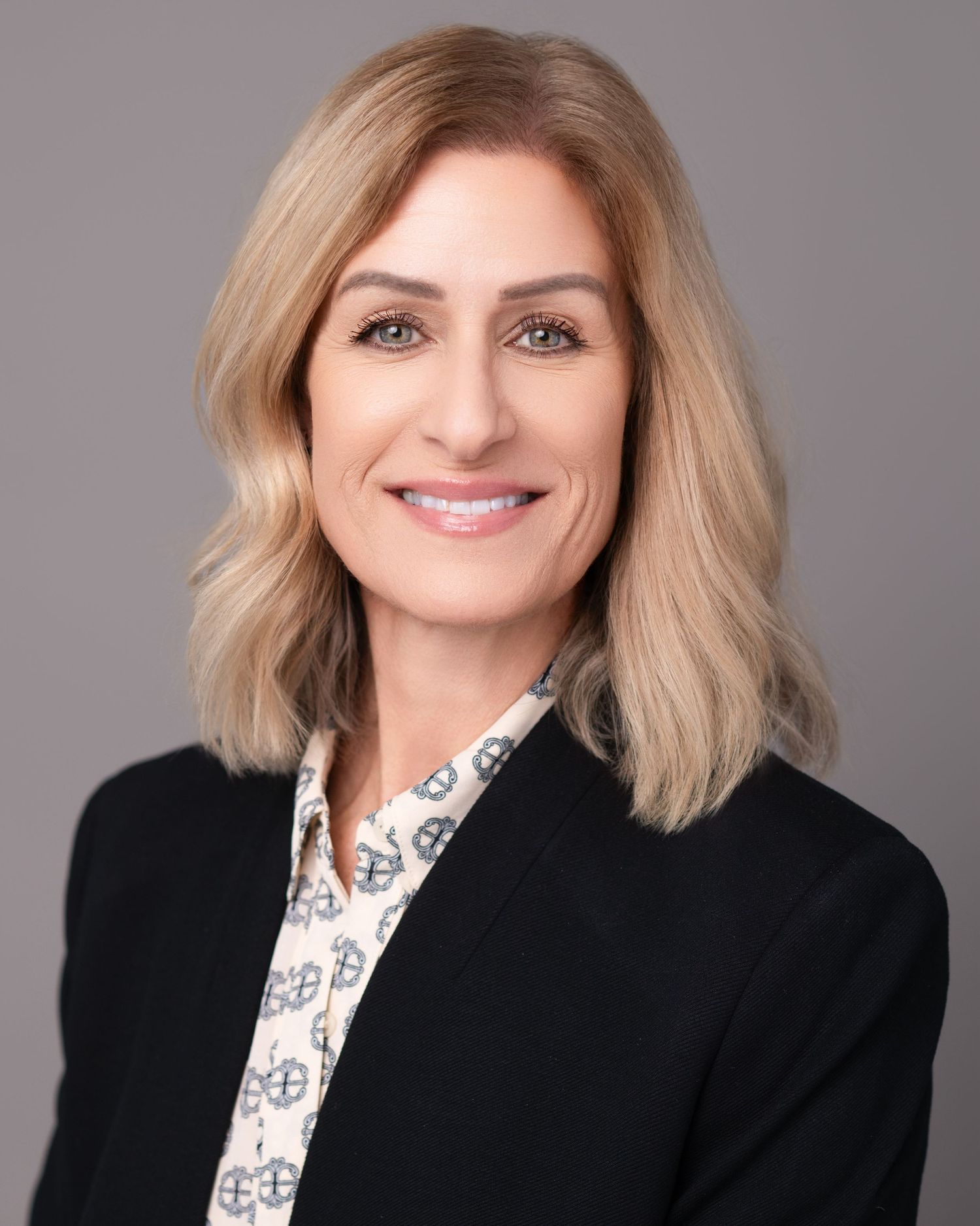 Professional headshot series showing a woman in a black blazer and patterned blouse against a gray background.