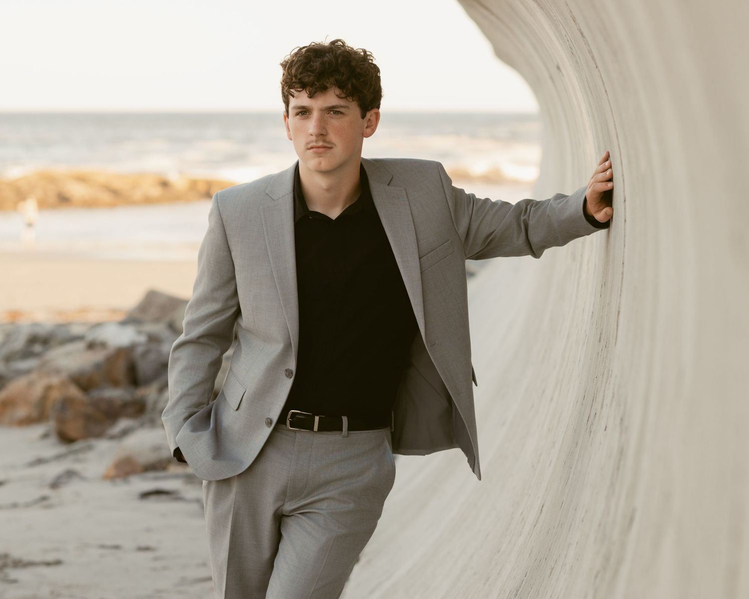 Casual professional leaning against white architecture in grey suit.