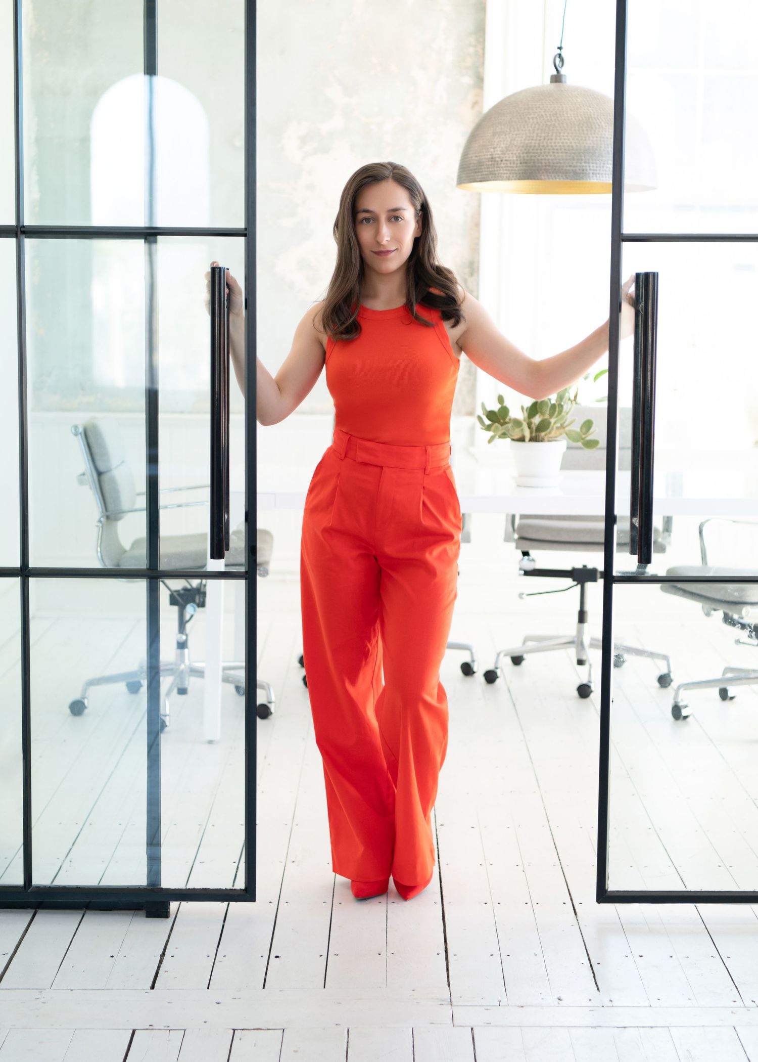Person in a bright red jumpsuit standing confidently in a modern white office space.
