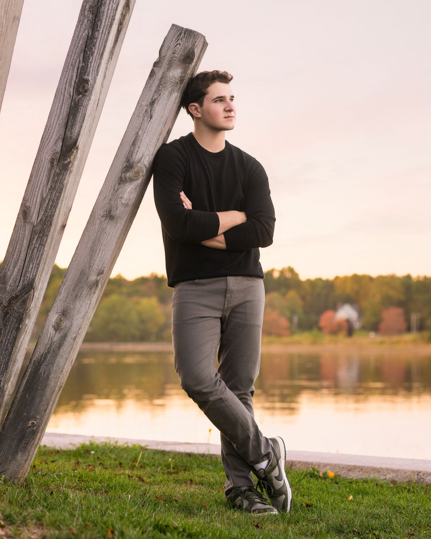 Person in black shirt and gray pants sitting by wooden posts at sunset near lake.