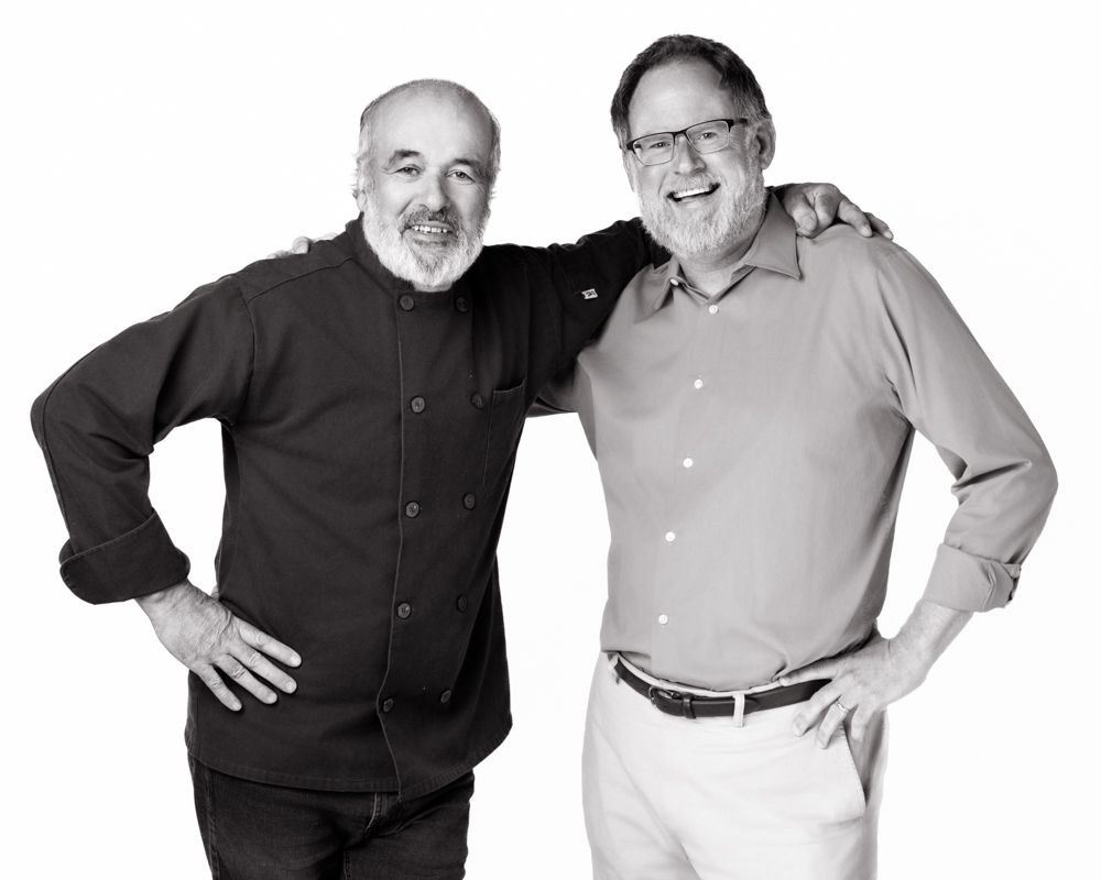 Two smiling men pose together in a black and white portrait, one in a dark shirt and one in a light button-up shirt. Amesbury MA studio