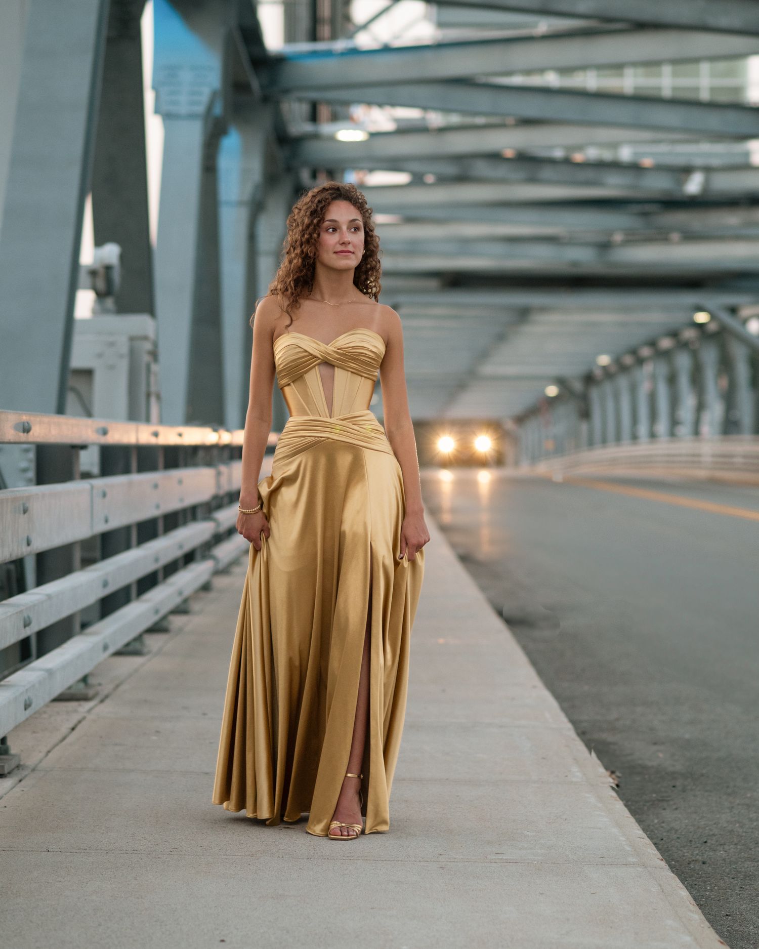Elegant portrait in a gold evening gown on an industrial bridge.