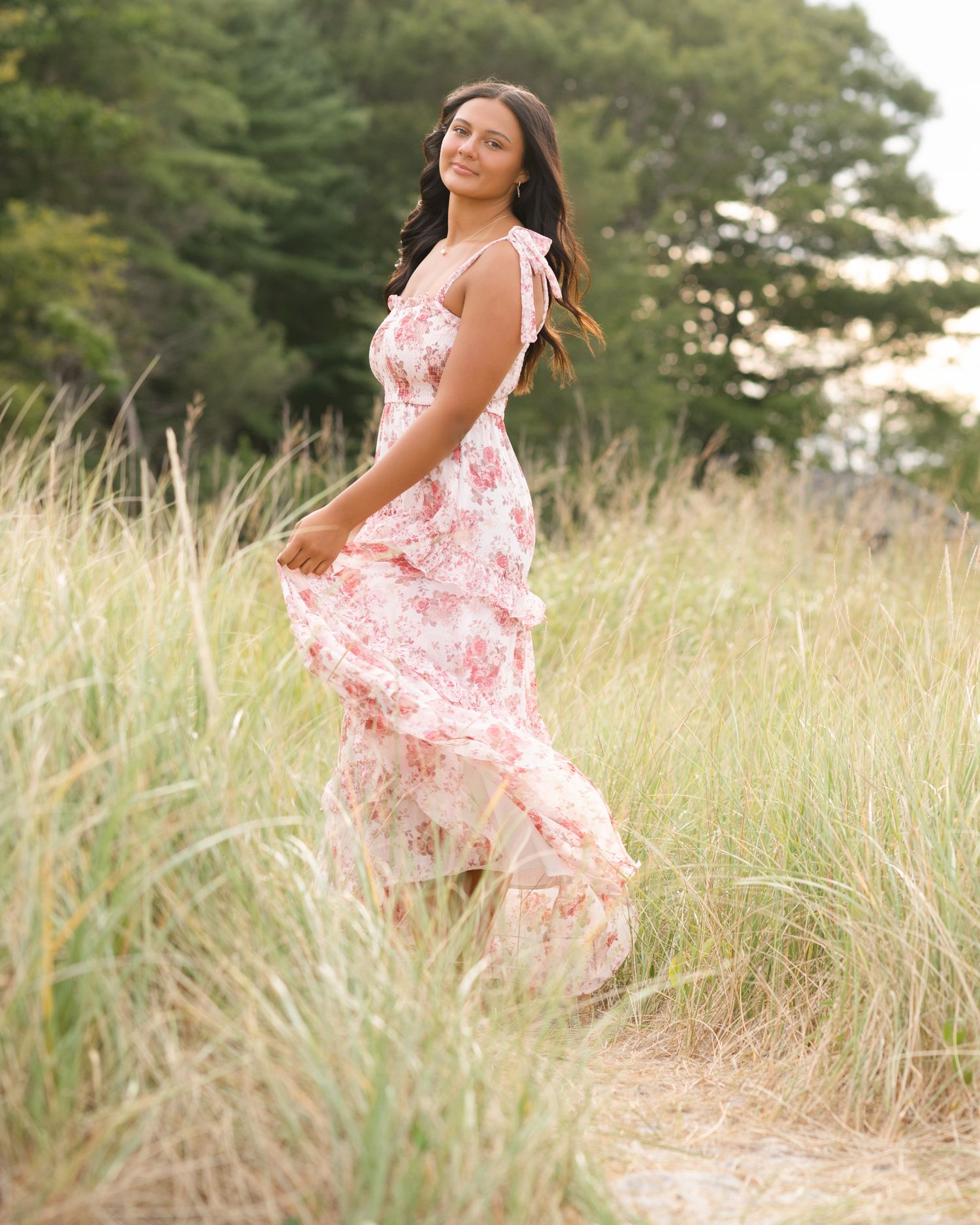 A flowing pink floral dress catches the breeze in a summer field portrait.