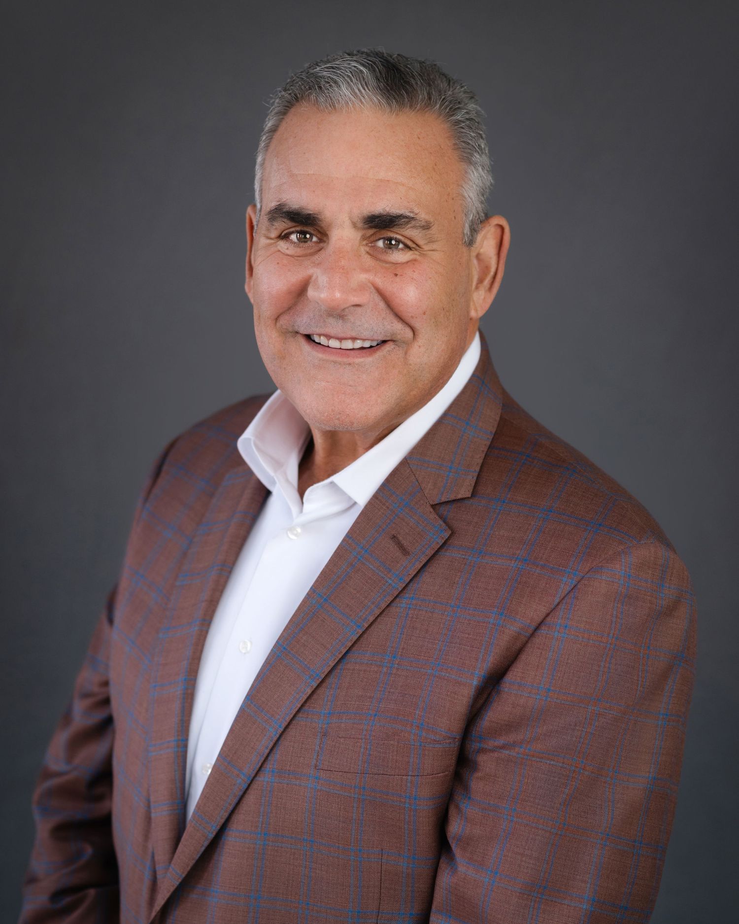 Business portrait of person in brown plaid blazer against dark background.