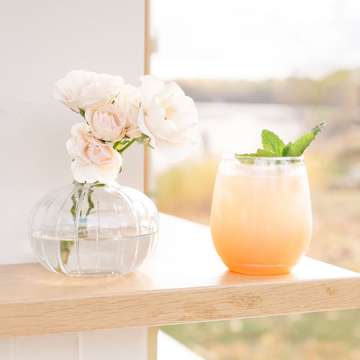 Soft focus still life of cocktails and flowers on wooden surface in natural light.