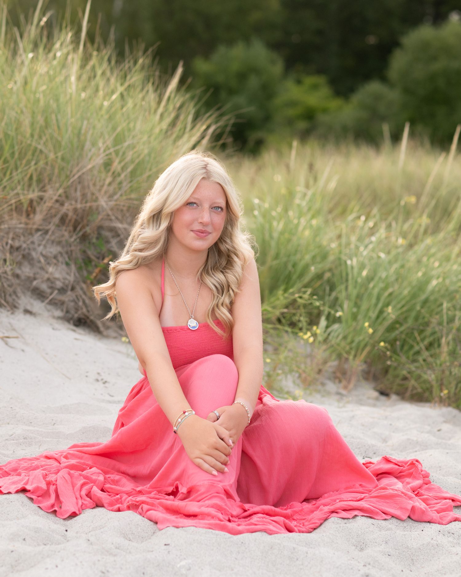 Beach portrait featuring a coral-colored flowing dress against coastal grass.