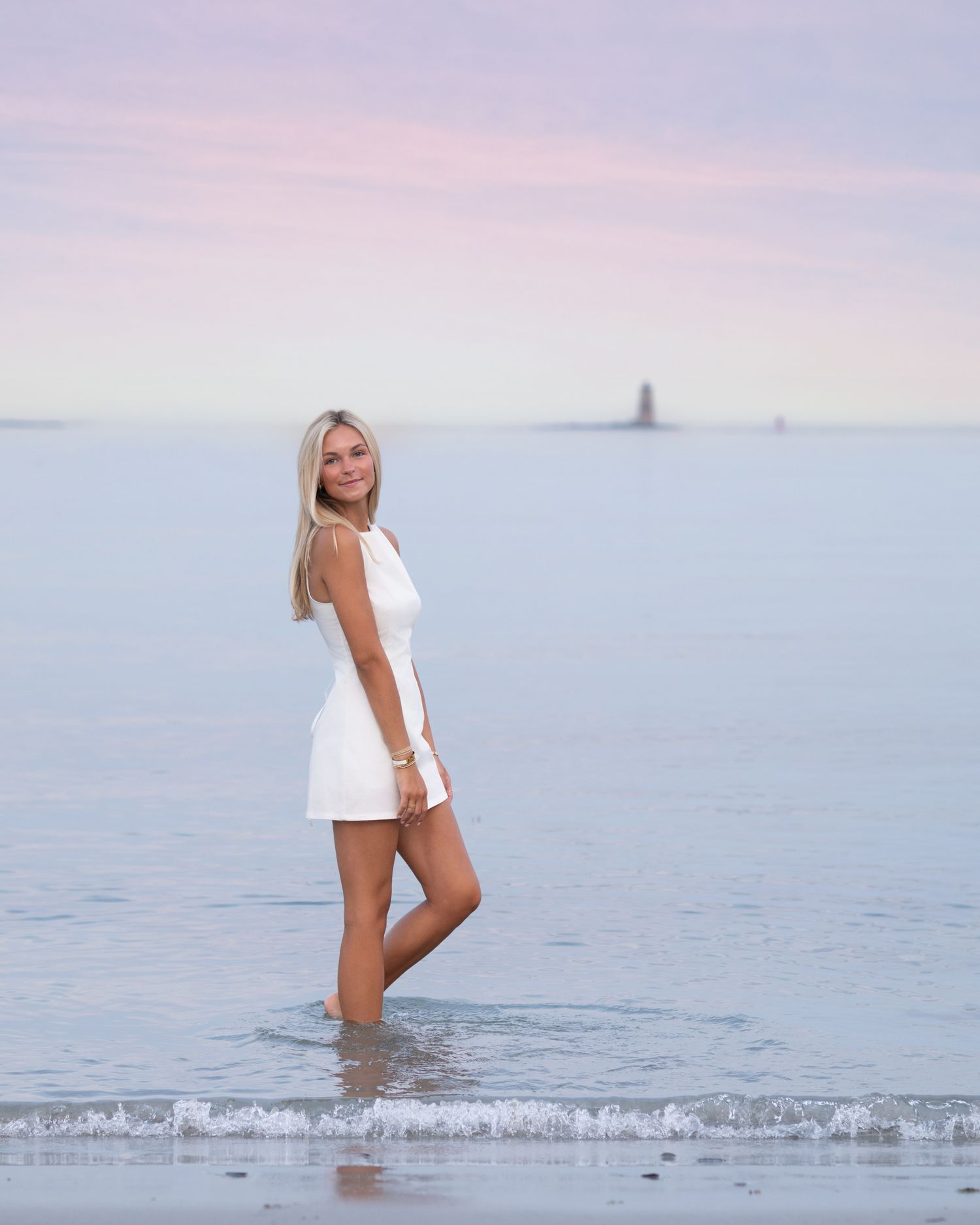 Woman in white swimwear walking through shallow ocean water at sunset.