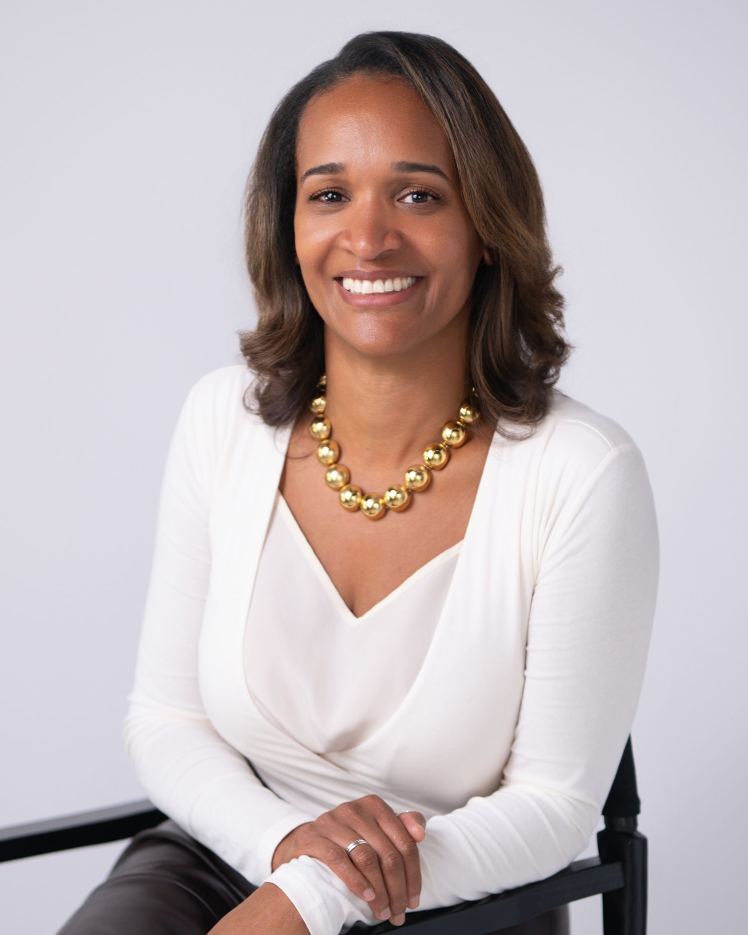 Professional headshot of someone wearing a white sweater and gold necklace against a light gray background. Amesbury, MA