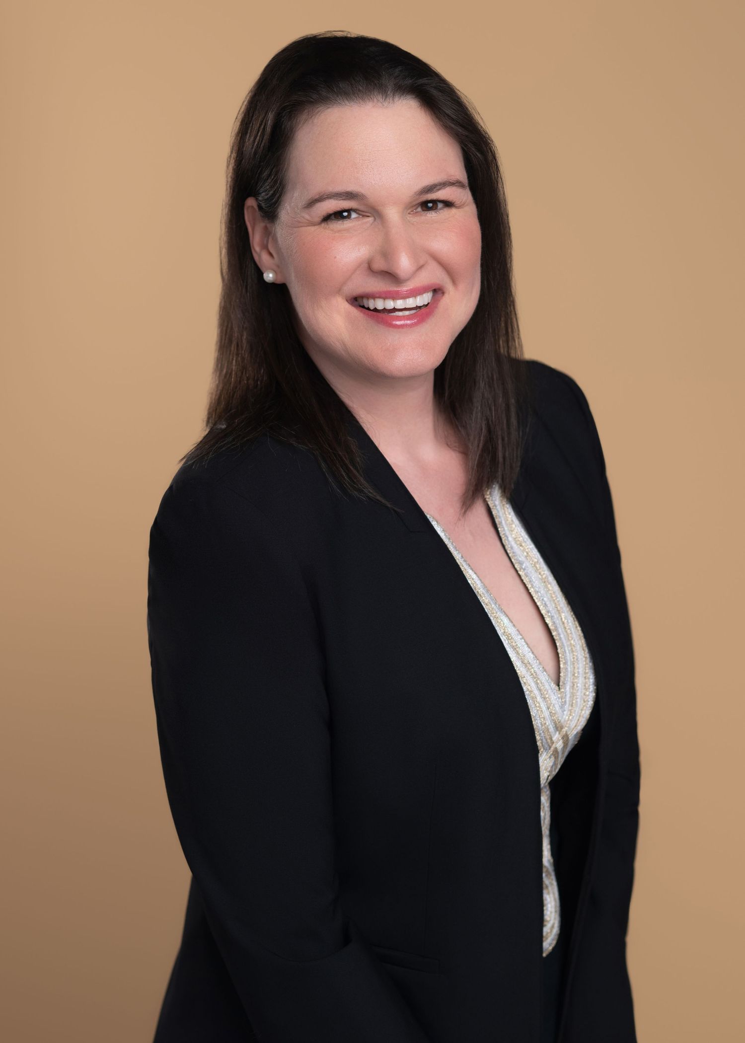 Professional headshot series in a black blazer against a warm beige background.