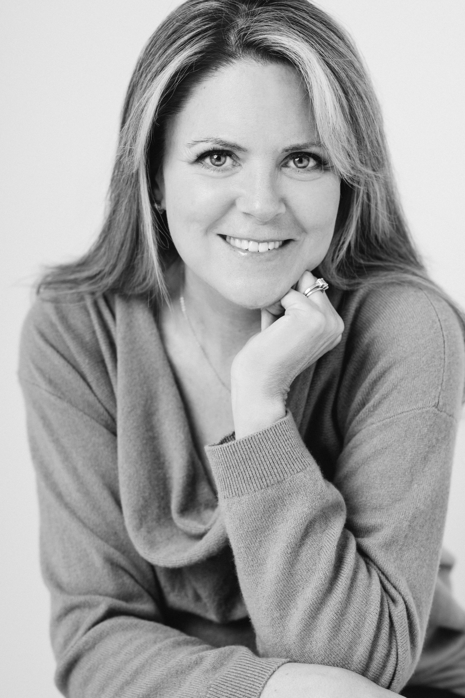 A series of five black and white portraits showing a woman in a gray sweater expressing different cheerful poses and emotions.