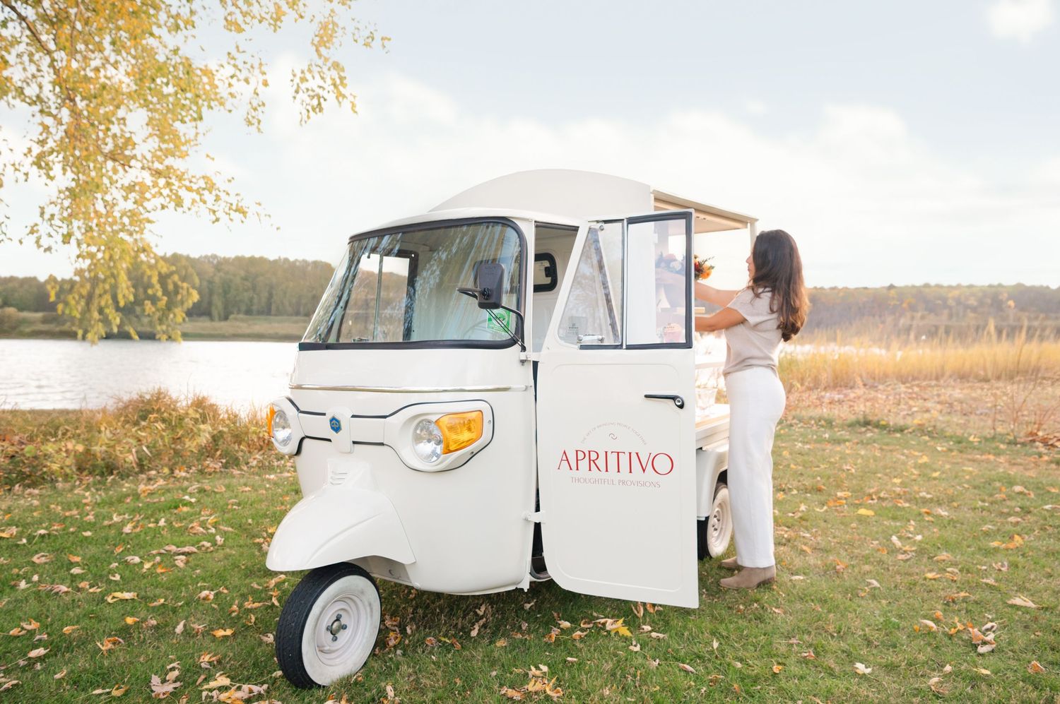 A vintage white photo booth camper van parked in an autumn field with golden leaves and trees in the background for an Amesbury MA Branding