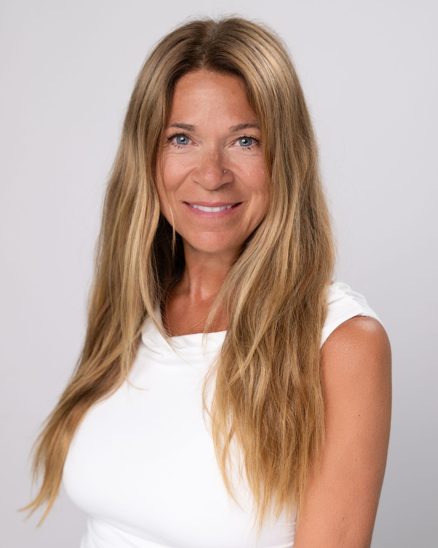 Professional headshot of person with long blonde hair wearing white sleeveless top.