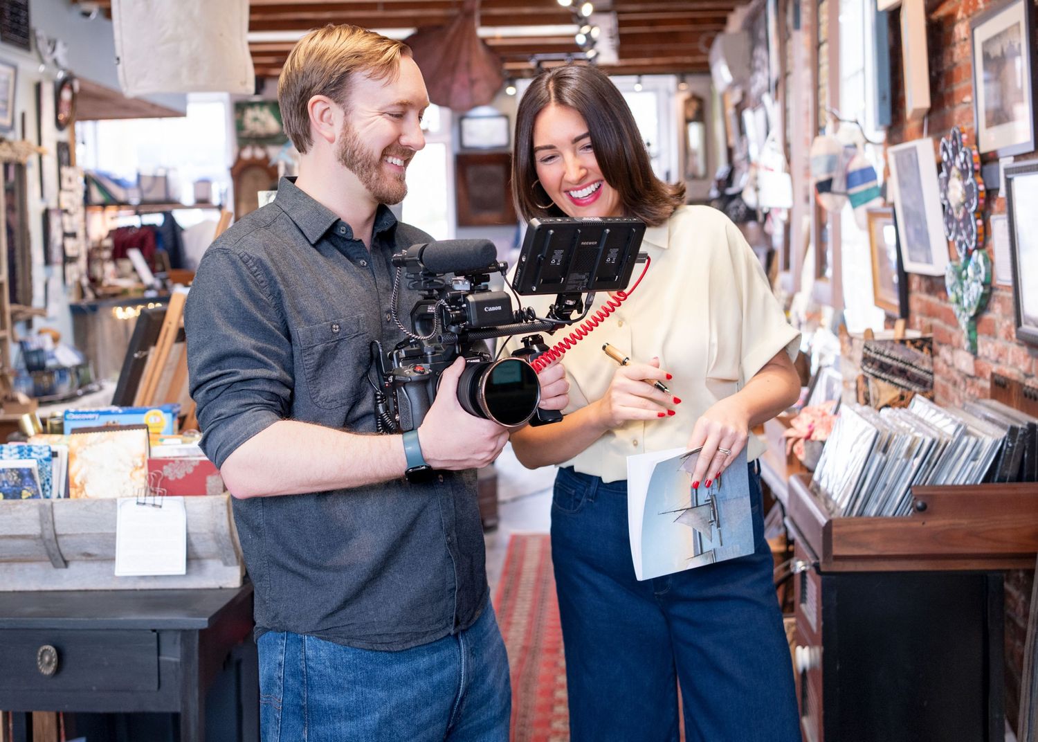 A man and woman smile while reviewing footage on a professional camera inside a charming vintage shop.