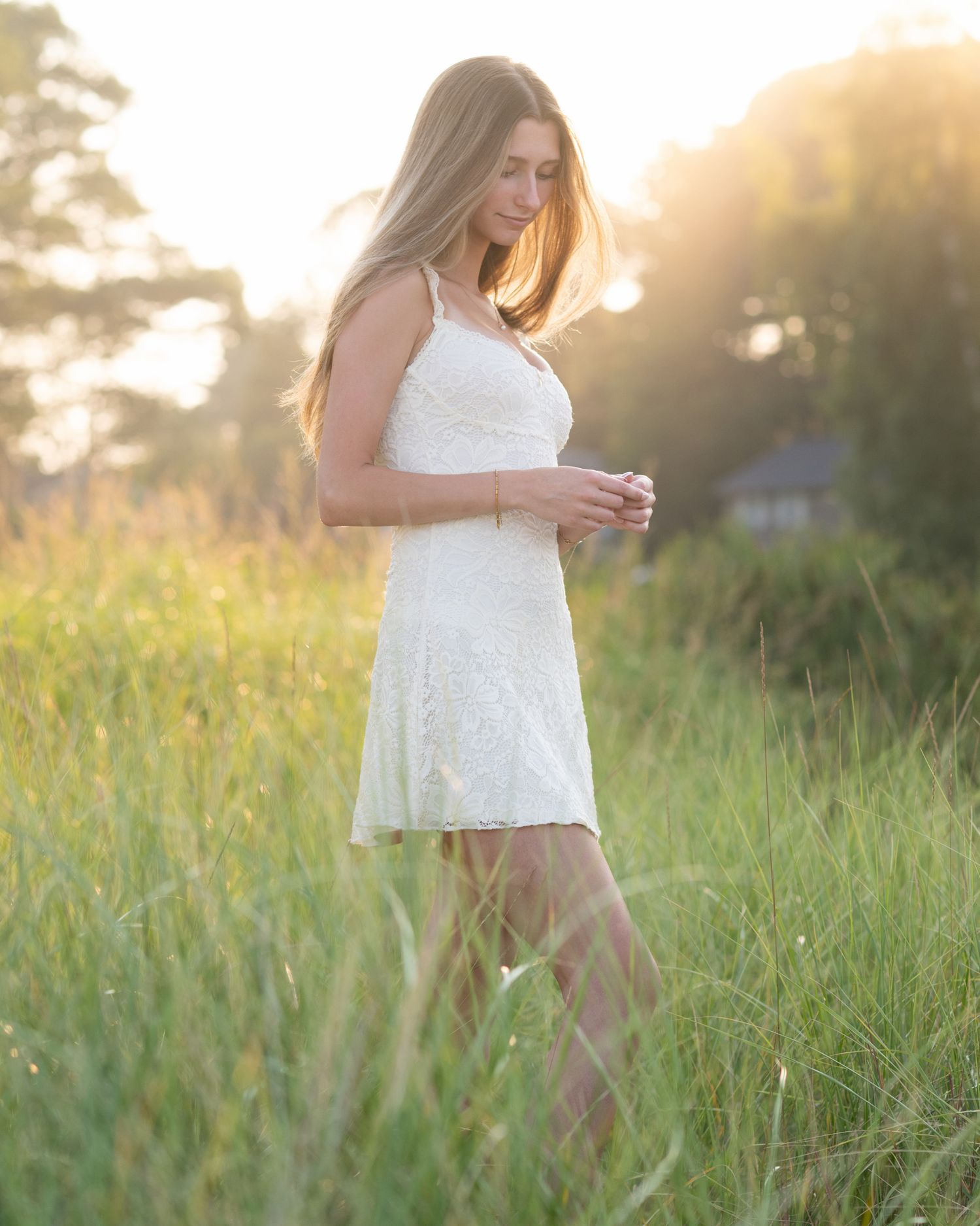 Ethereal portrait in white dress among tall grass during sunset.