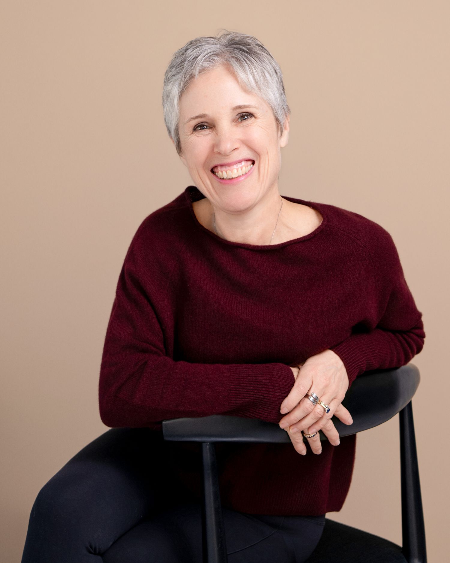 Professional portraits showing warm smiles in burgundy sweater against neutral backdrop.