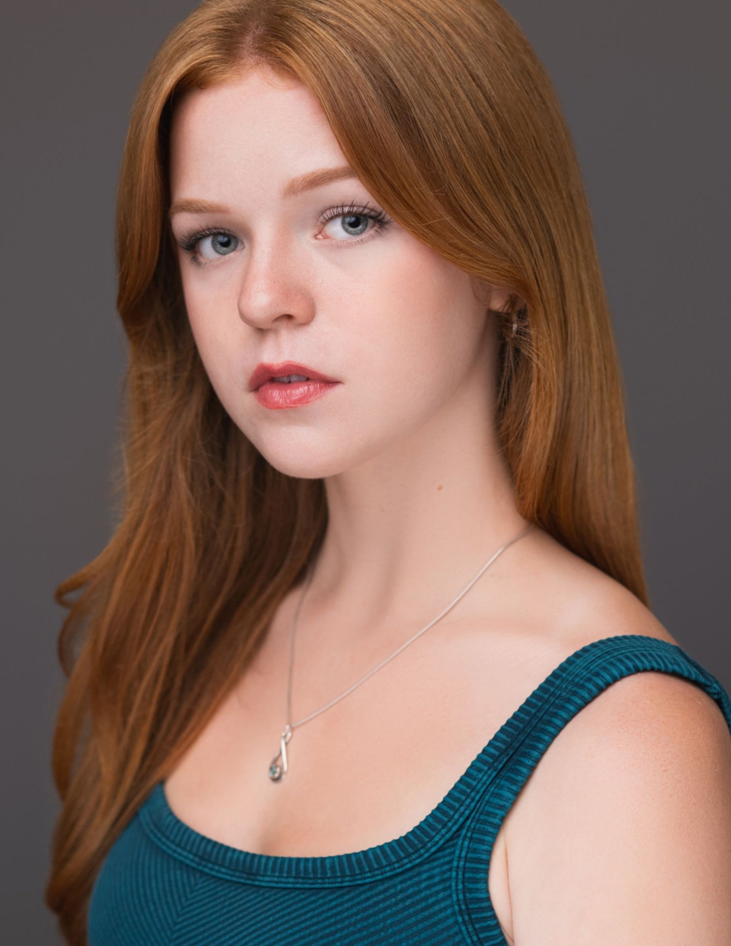 A person with red hair wearing a teal tank top poses against a gray backdrop in a series of close-up Headshot.