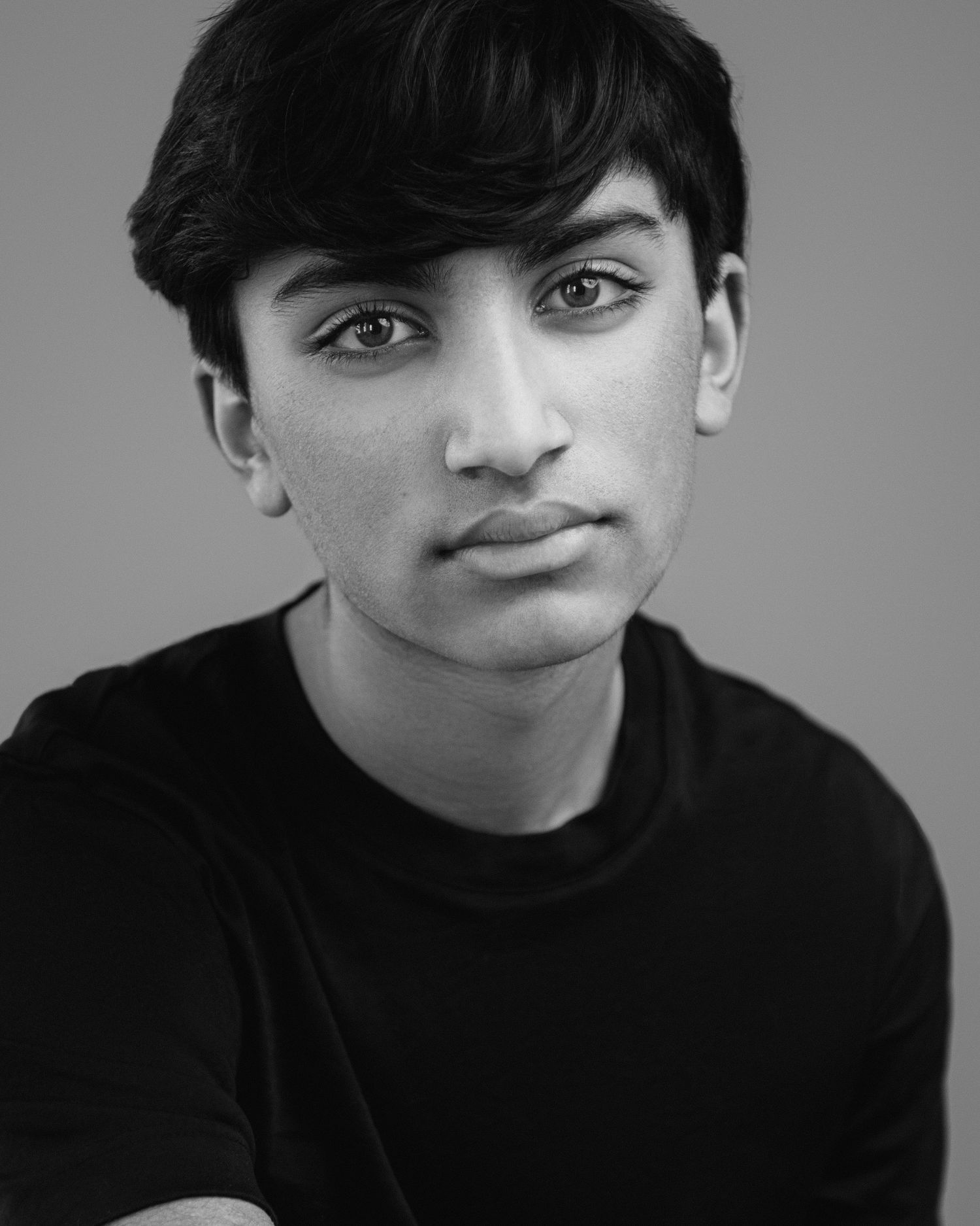 Black and white portrait of a person in a dark top with striking features against a simple background.