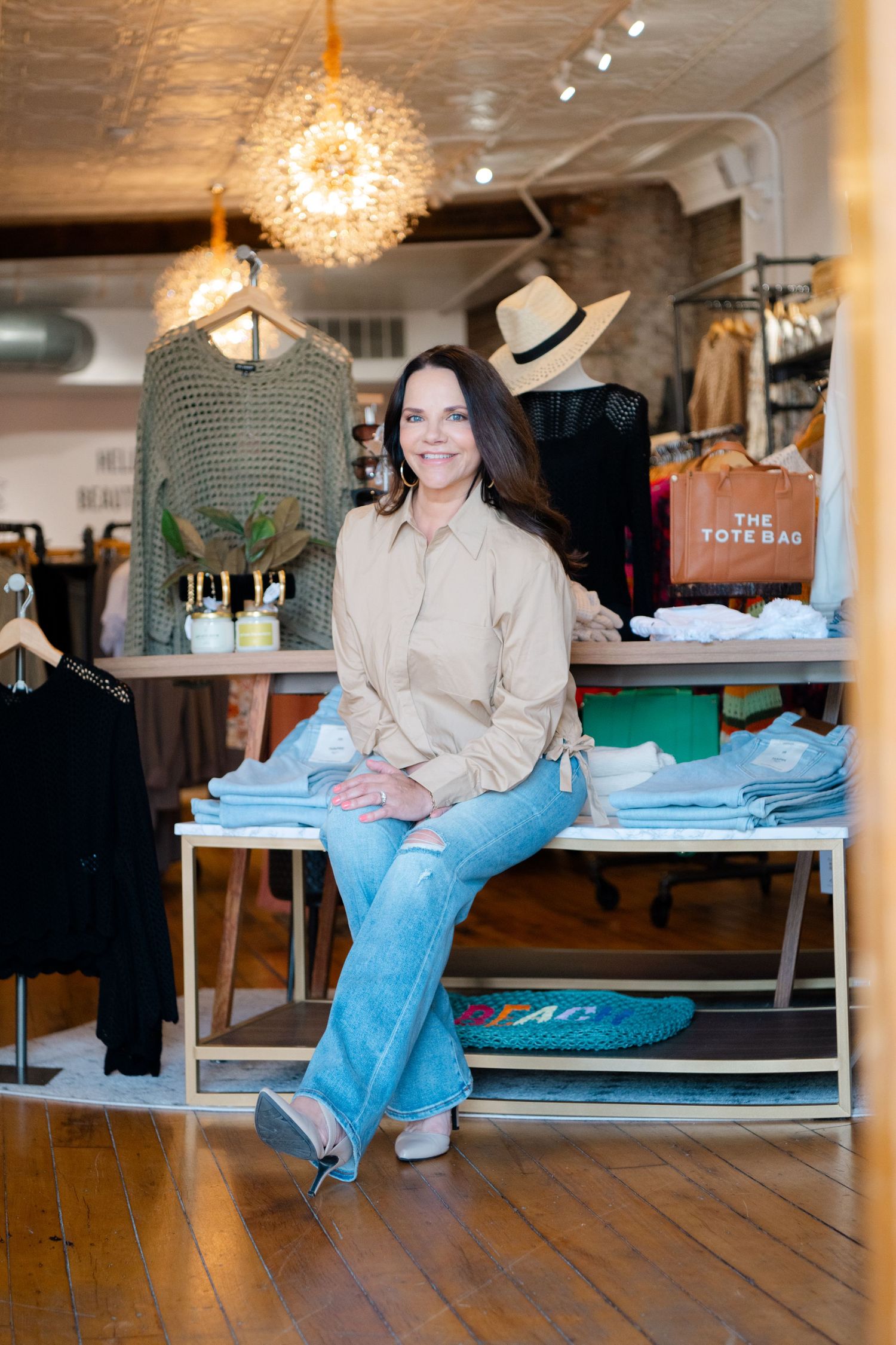Retail boutique in Amesbury MA, interior with wooden floors, clothing displays, and a sparkly chandelier in a modern shopping space.